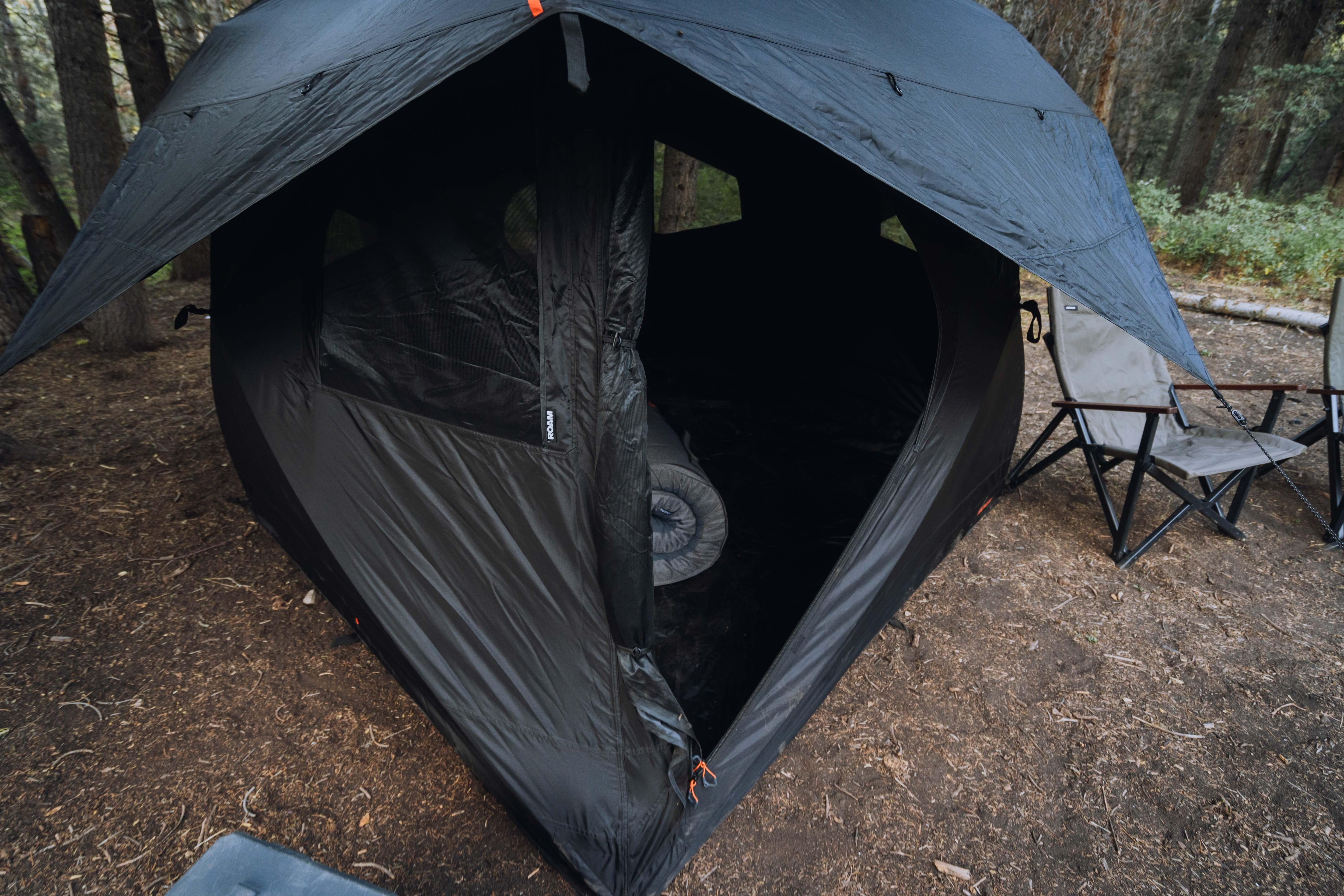 Overlanding camping tent with open door, camp chair, set up in forest setting