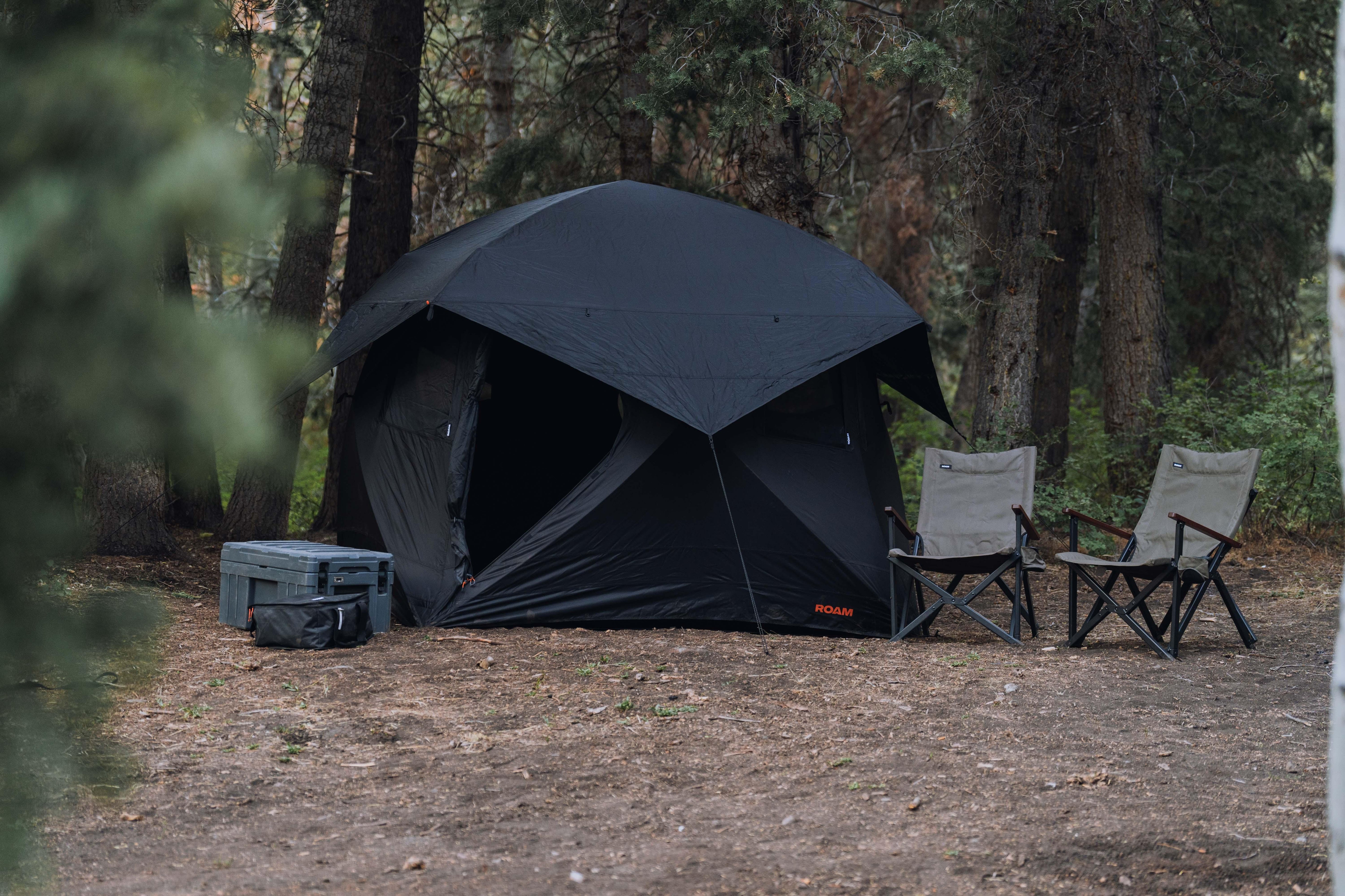 Black Roam dome tent with camping chairs and storage boxes in a forest campsite setting