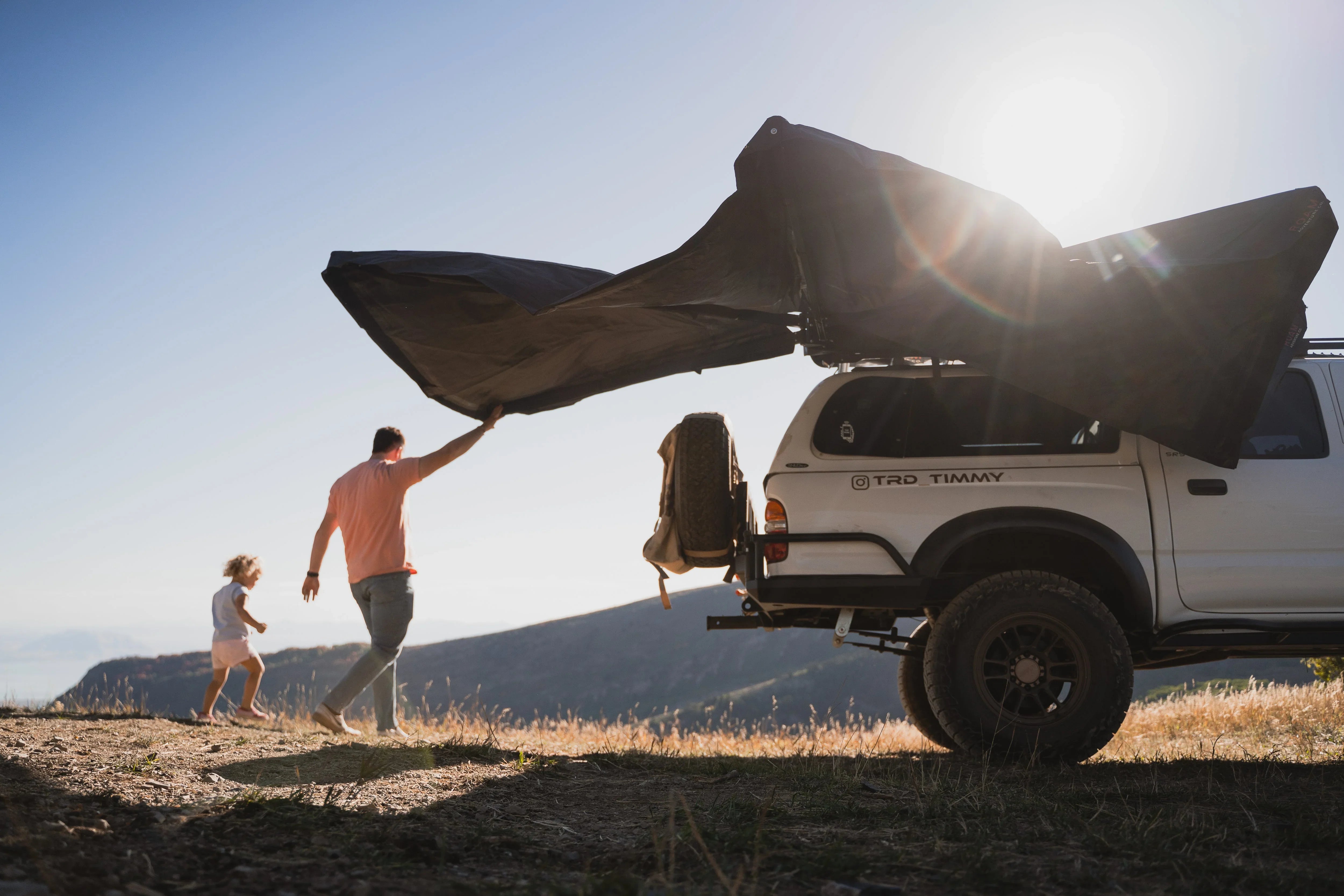 Man and child camping with Toyota 4Runner, awning extended, mountain backdrop, overlanding adventure