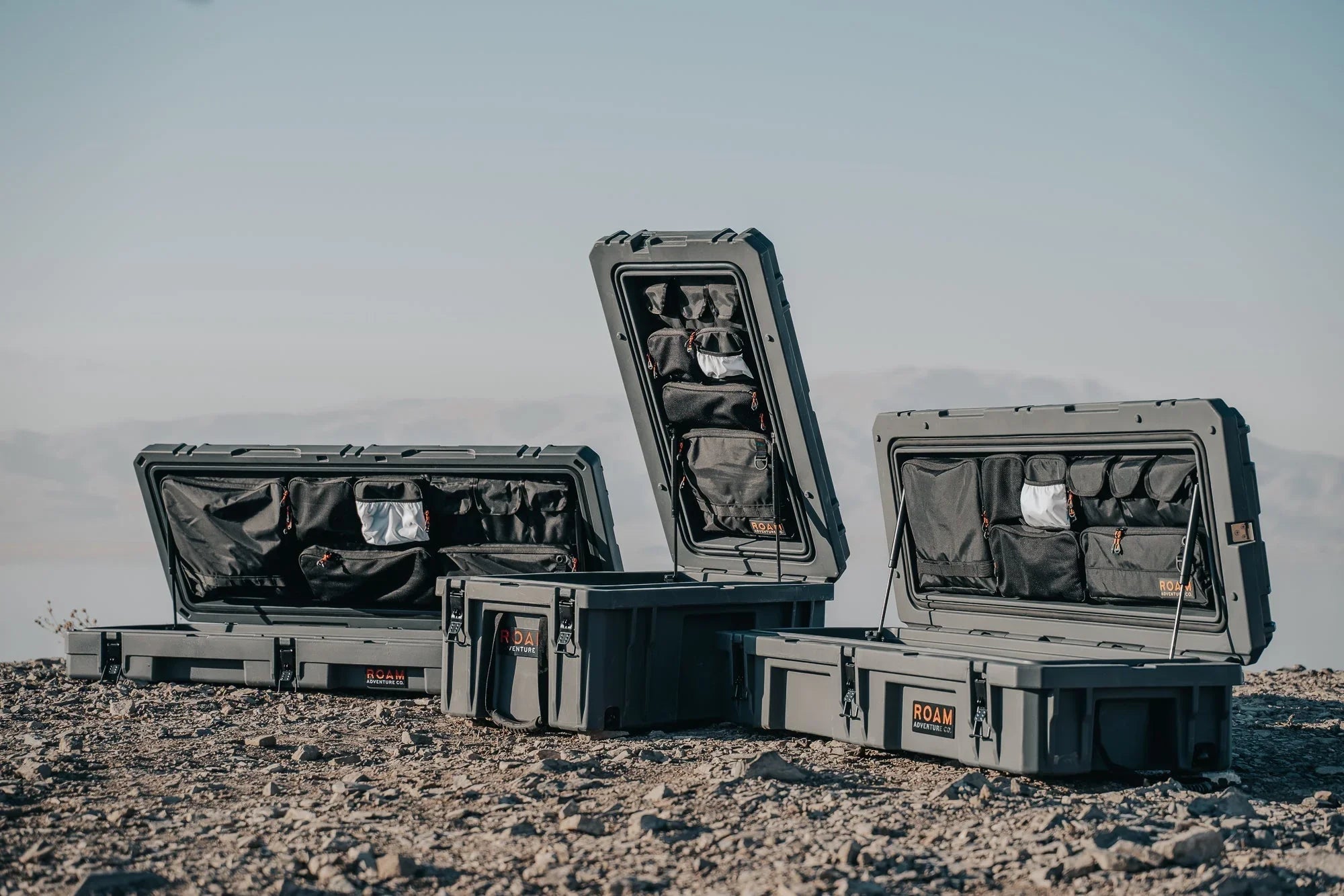 Rugged hard storage cases with open lids and interior pockets, set outdoors on rocky ground