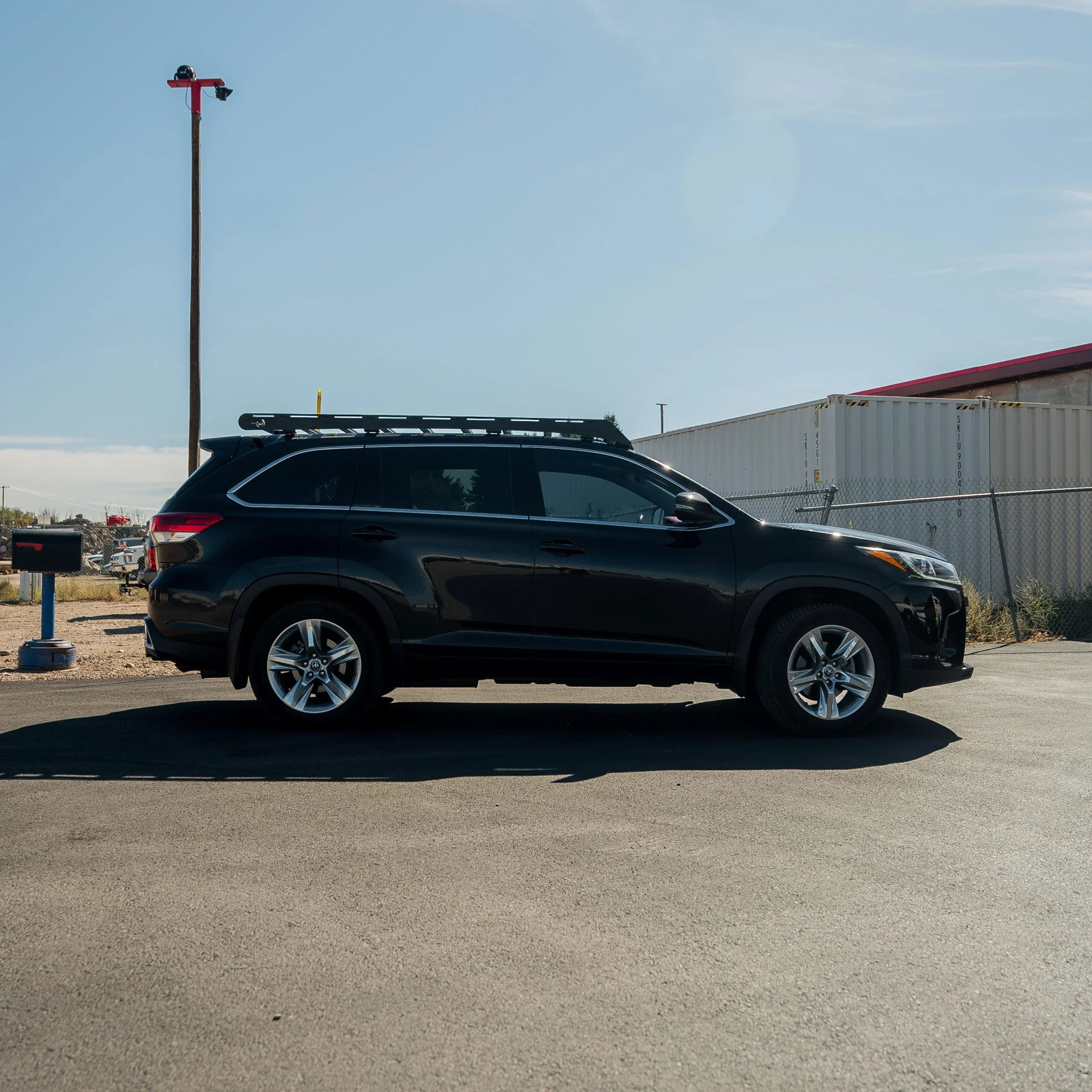 Black Toyota Highlander with roof rack parked outdoors, suited for overlanding gear