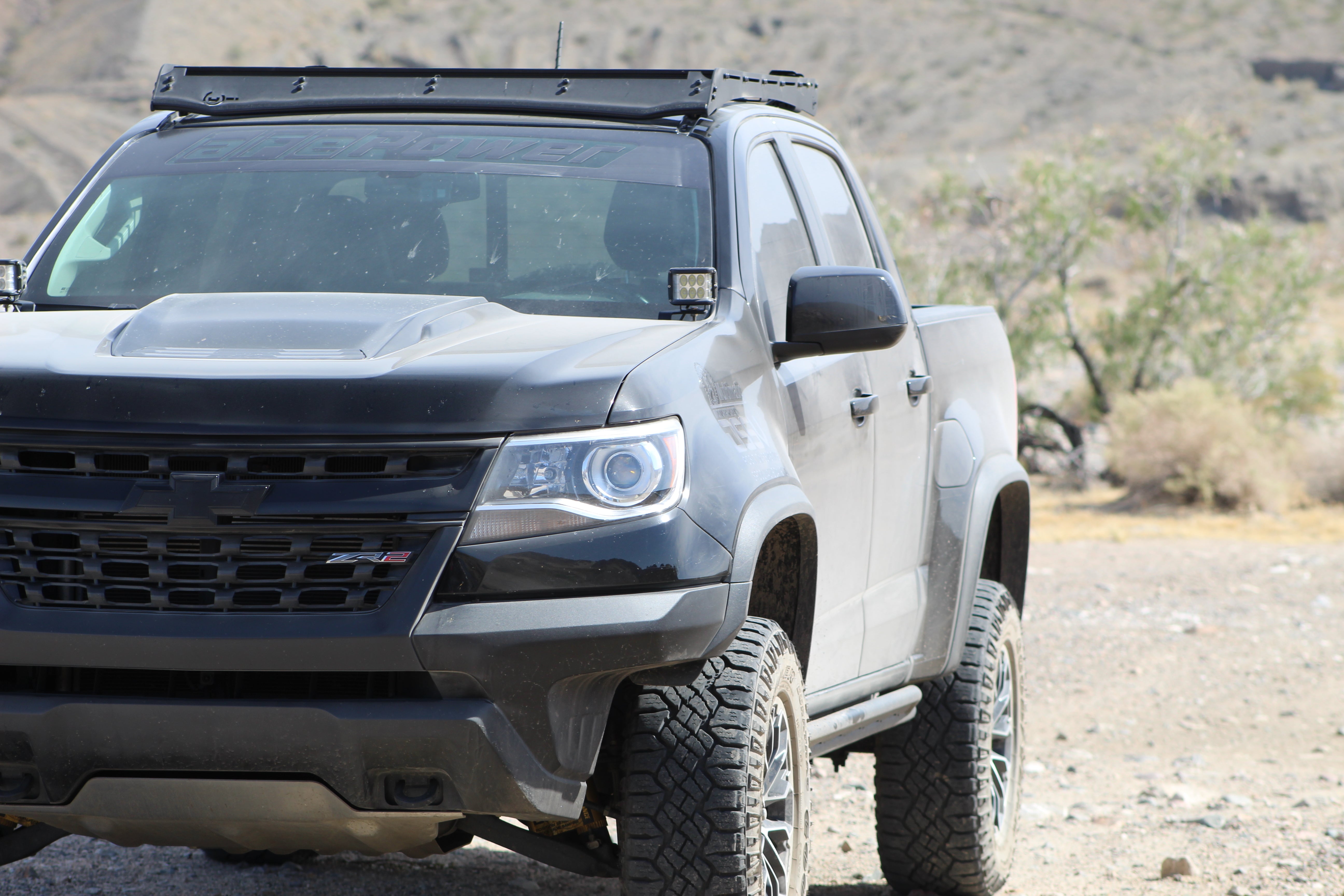 Lifted black Chevy ZR2 off-road truck with roof rack and LED lights in a desert setting