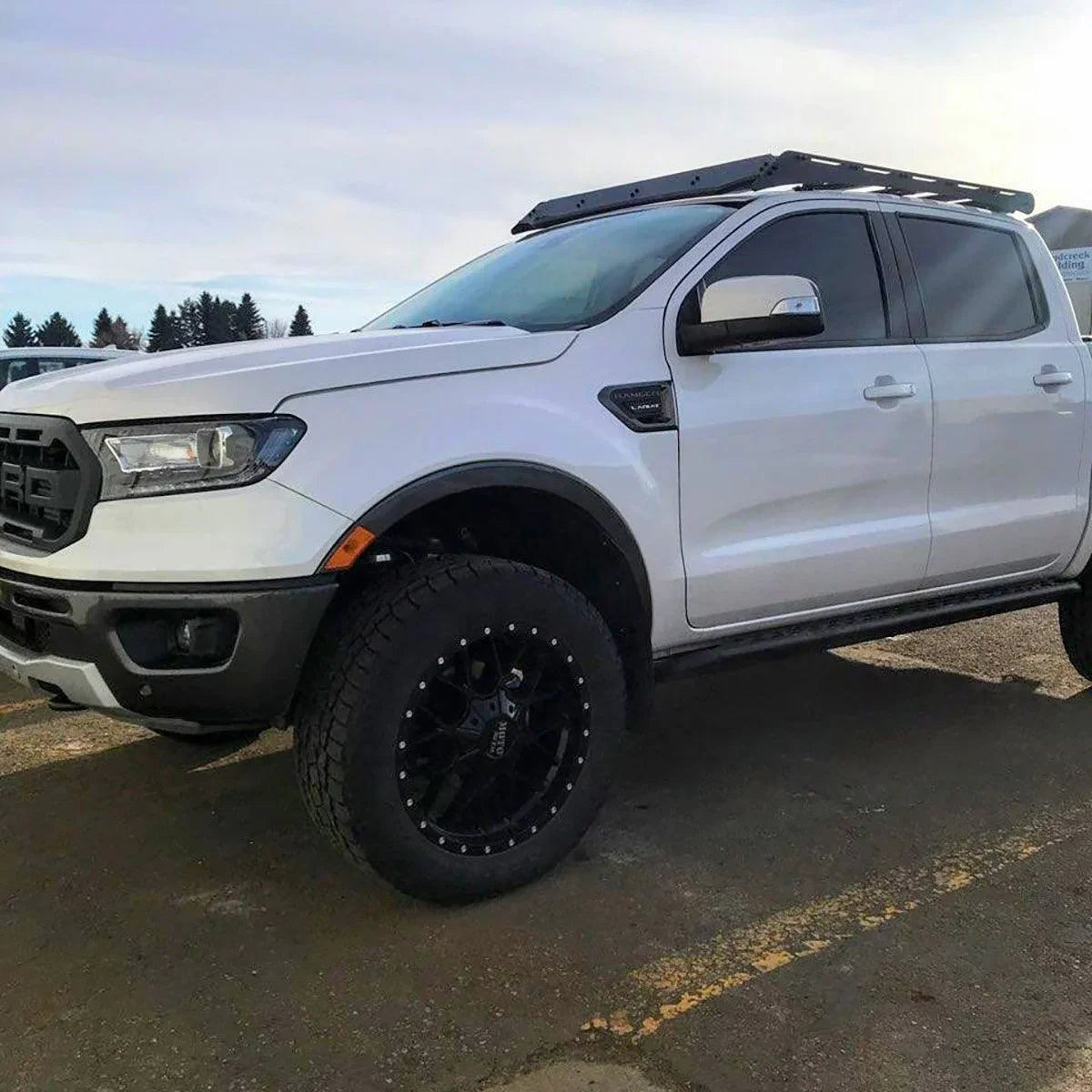 White Ford Ranger with black roof rack and off-road tires, parked outdoors