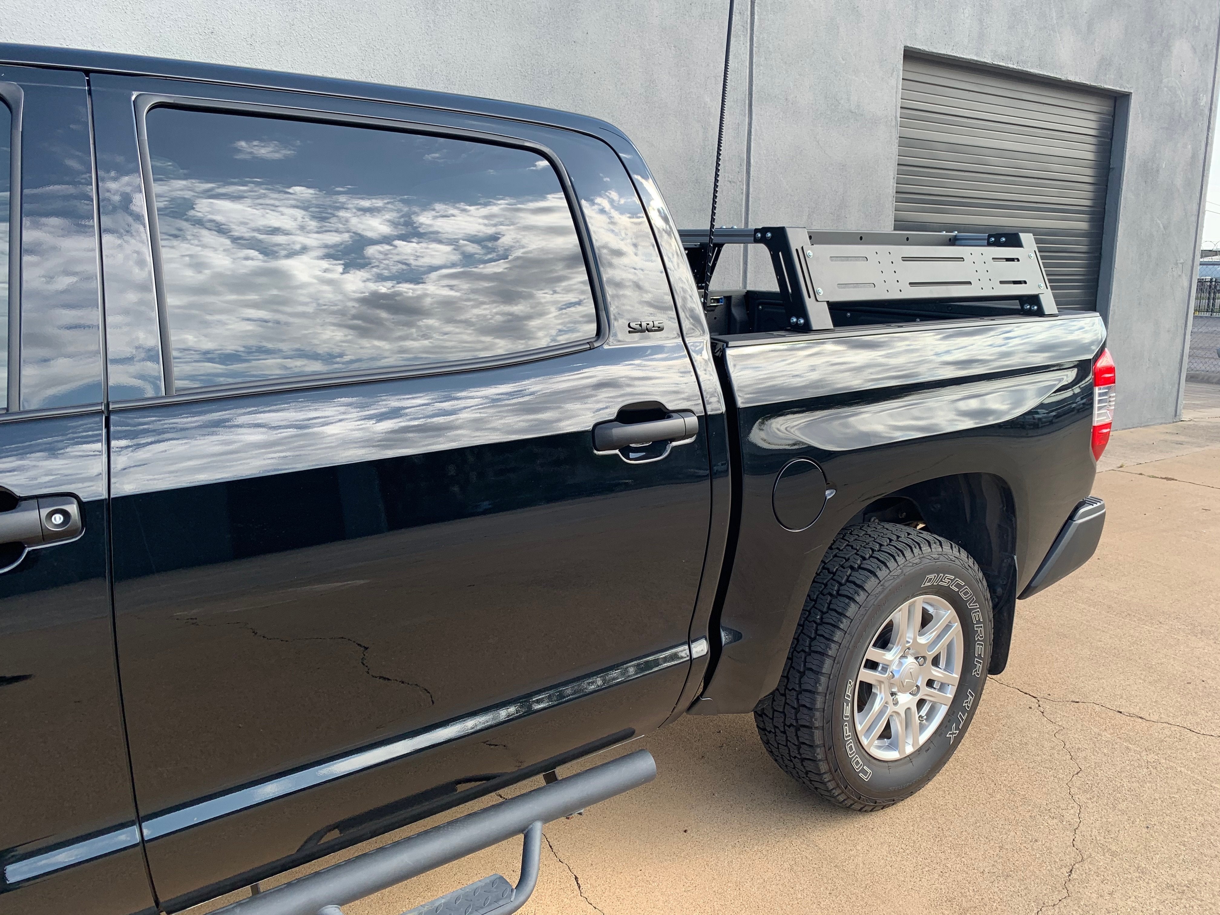 Black Toyota pickup truck with overlanding bed rack and rugged tires in outdoor setting