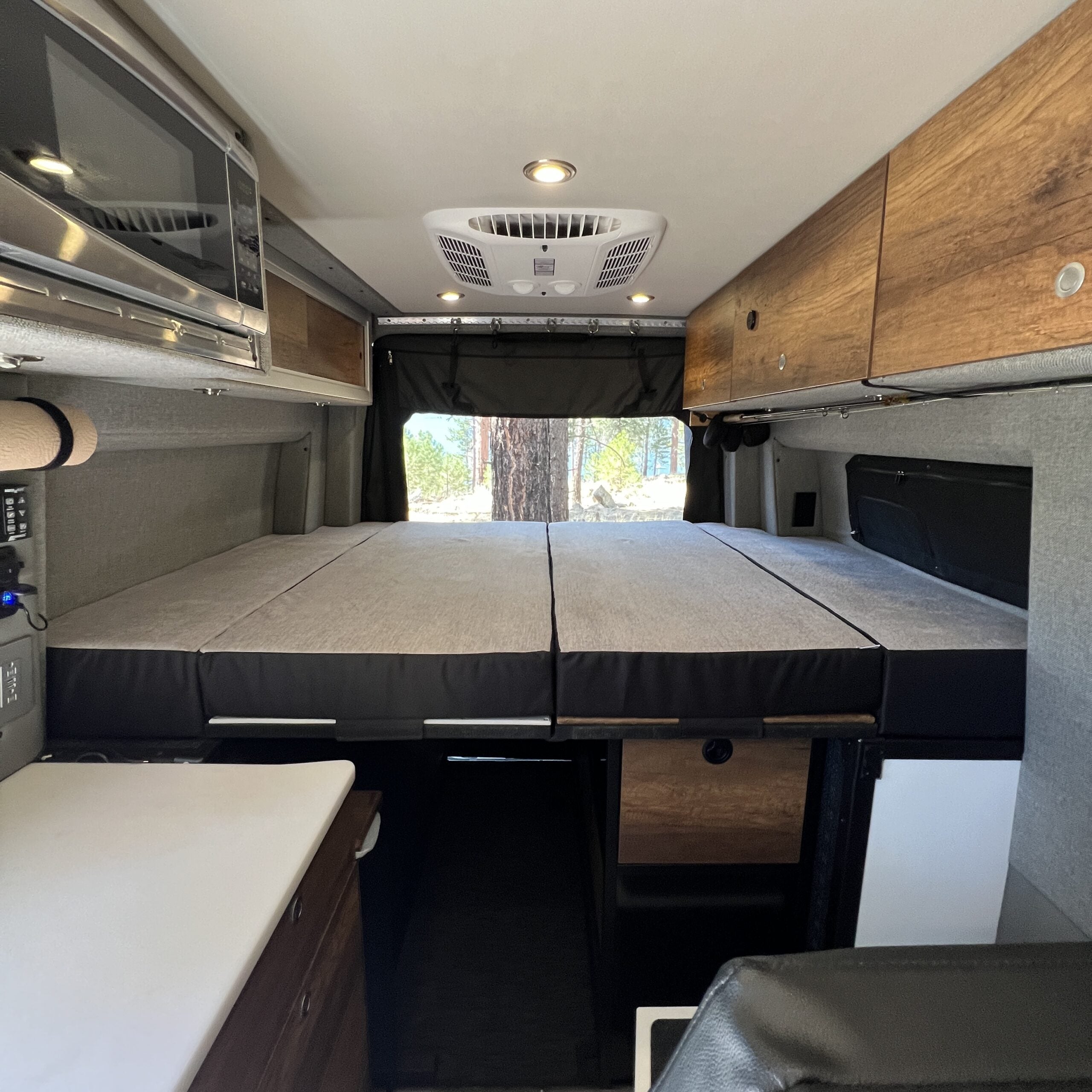 Interior of overland camper van with fold-out bed, storage cabinets, and built-in microwave