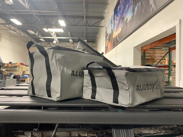 Two gray overland gear storage bags with black zippers on a vehicle roof rack in a warehouse