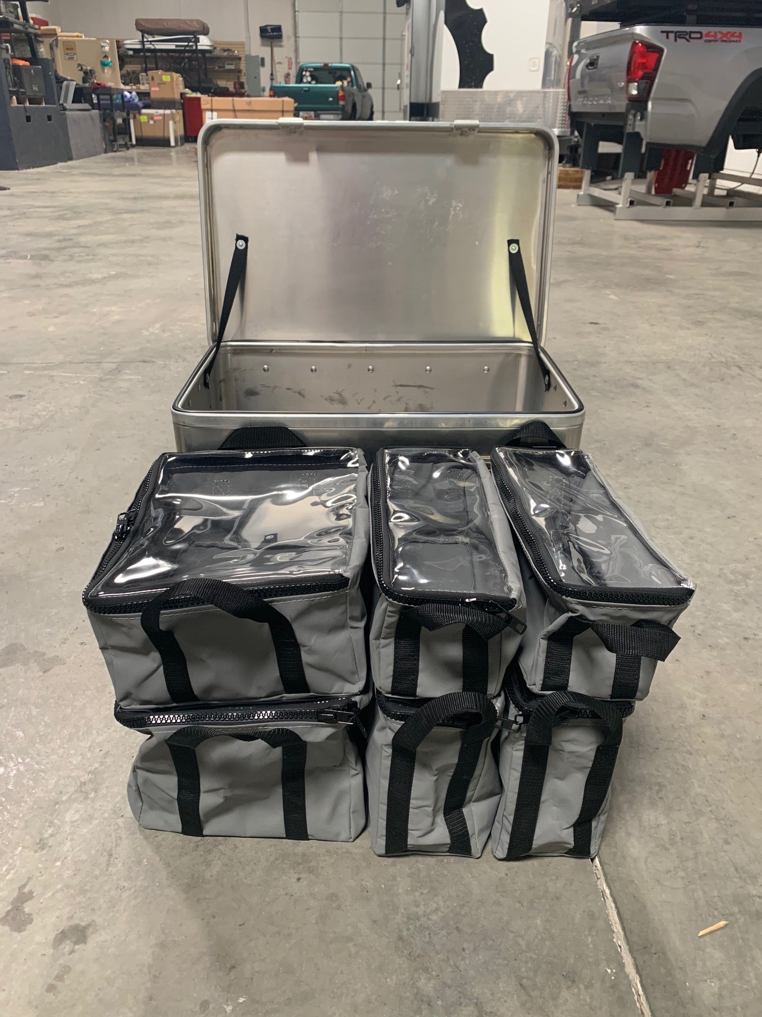 Aluminum storage box with six gray camping gear organizer bags in a garage setting