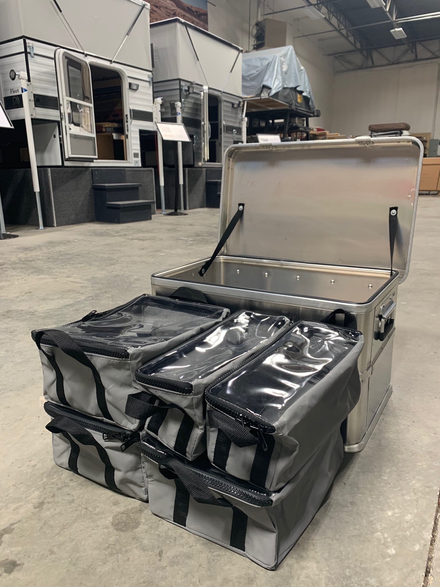 Overland camping aluminum storage box with four gray organizer bags, RV trailers in background