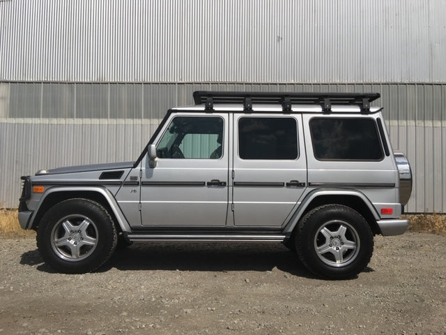 Silver off-road SUV with roof rack parked outdoors, adventure vehicle accessories visible