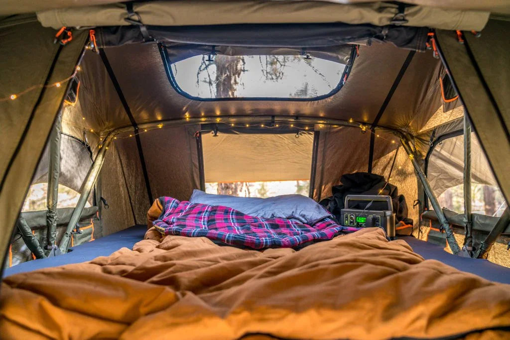 Cozy rooftop tent interior setup with bedding, string lights, and portable power station for overlanding
