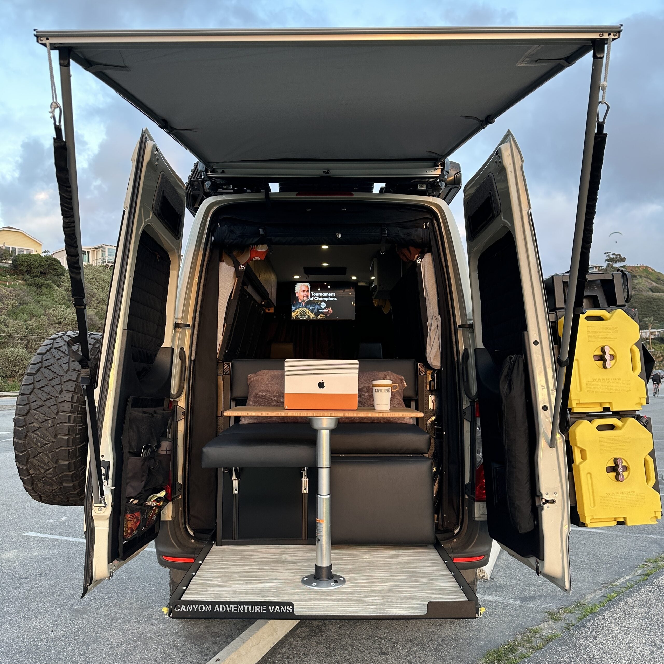 Overland camper van rear view with open doors, outdoor gear, worktable, and adventure setup