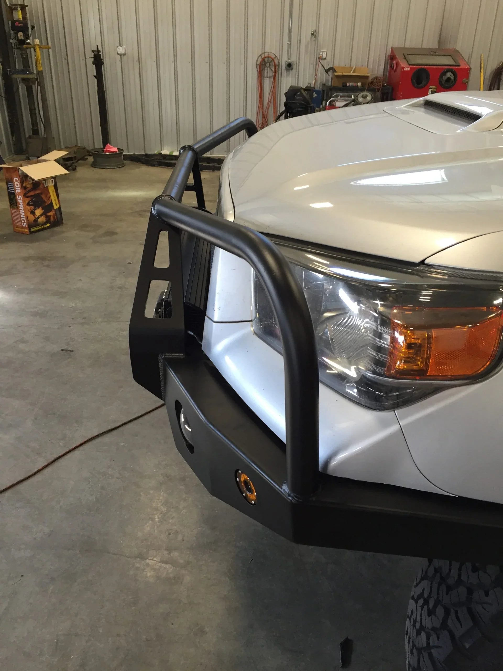 Steel off-road front bumper with grille guard installed on a Toyota Tacoma in a garage