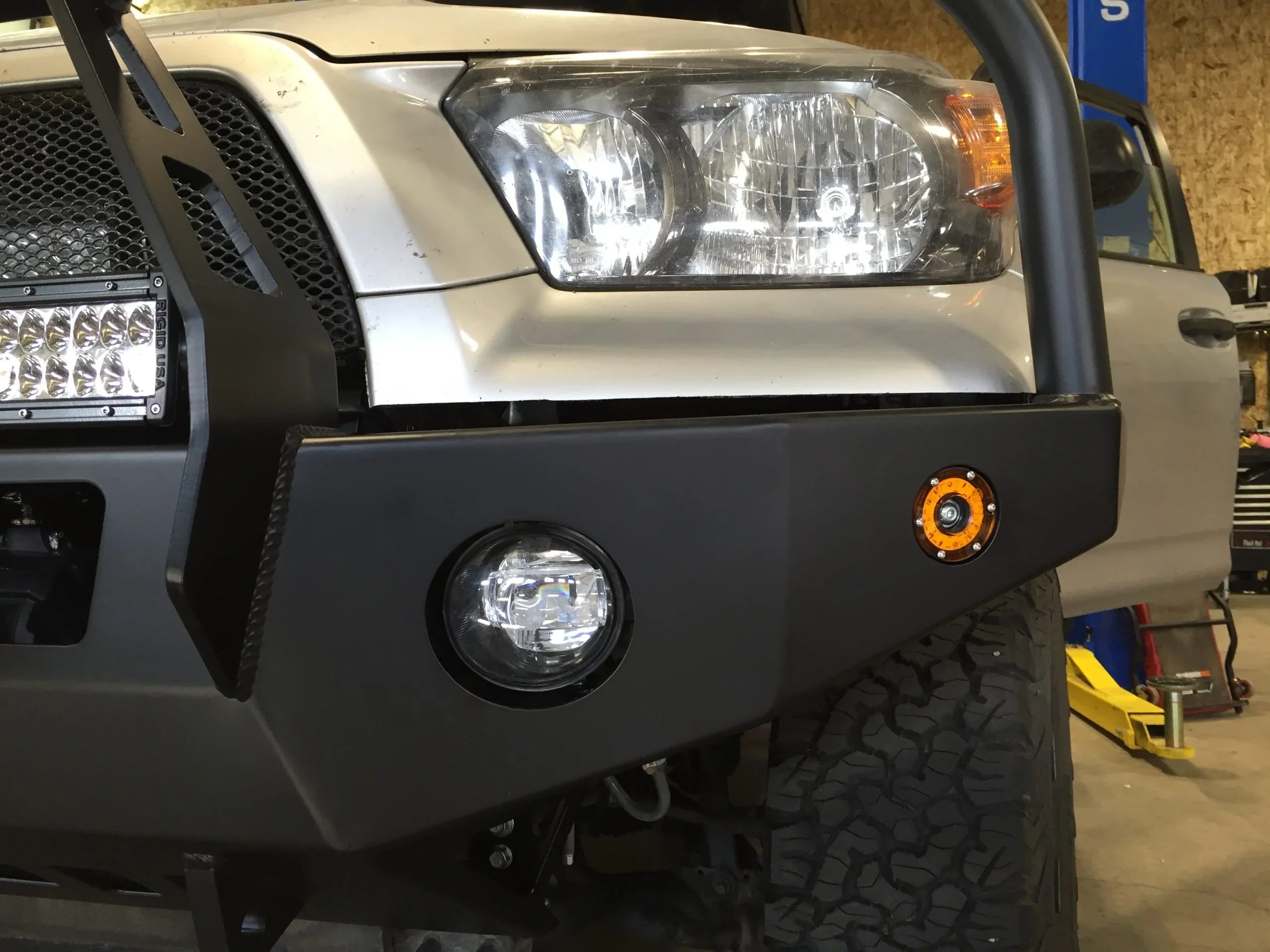 Toyota Tacoma with aftermarket steel front bumper, off-road tires, LED light bar, and fog lights