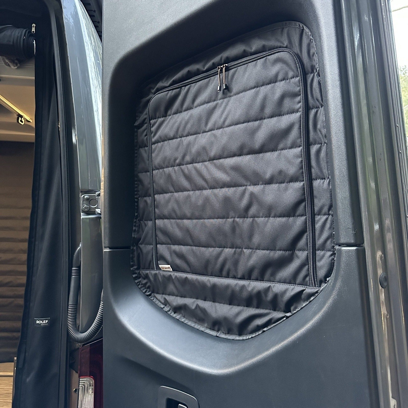 Insulated black quilted window cover installed inside camper van door, overlanding accessory
