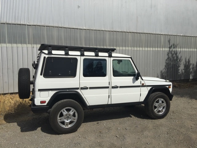 White off-road SUV with roof rack parked on gravel, ideal for overlanding and camping gear