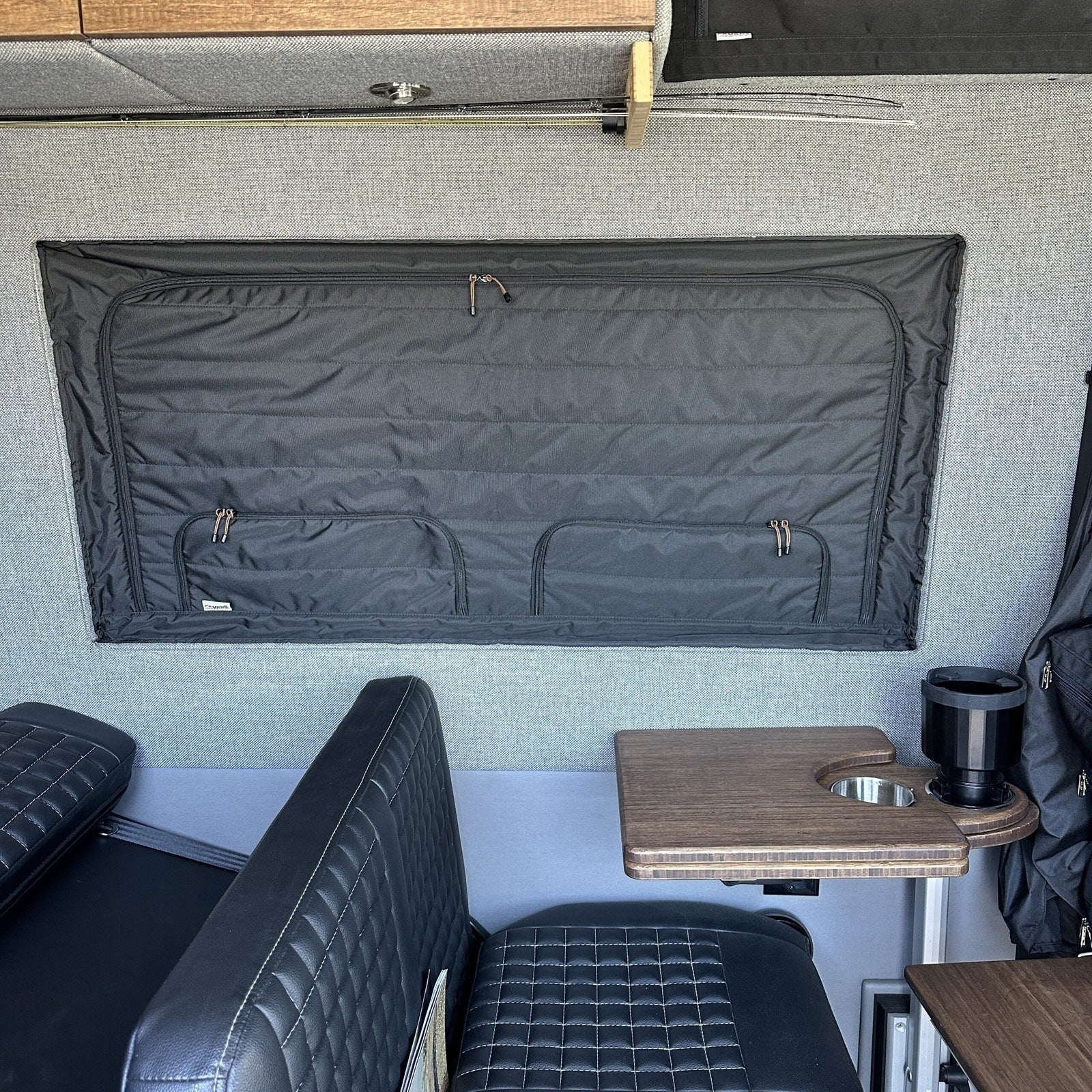 Padded window cover in a camper van interior with quilted seats and fold-out table