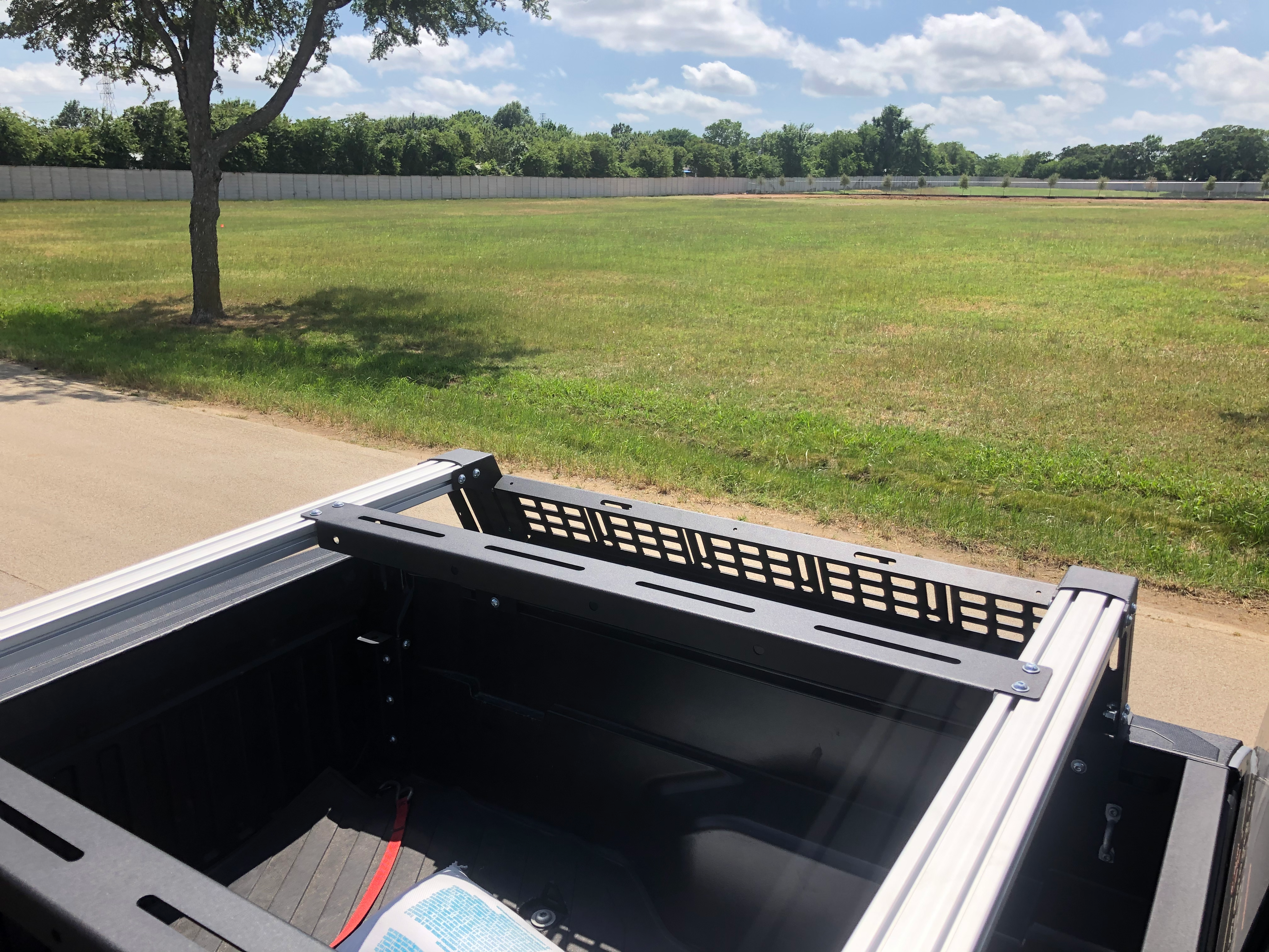 Overland truck bed rack on pickup parked by grassy field under blue sky
