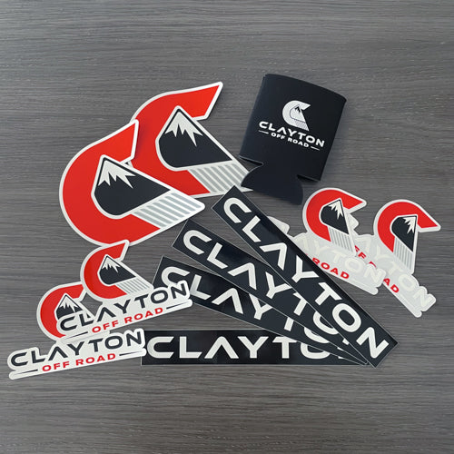 Clayton Off Road adventure vehicle decals and black can koozie on gray wood surface
