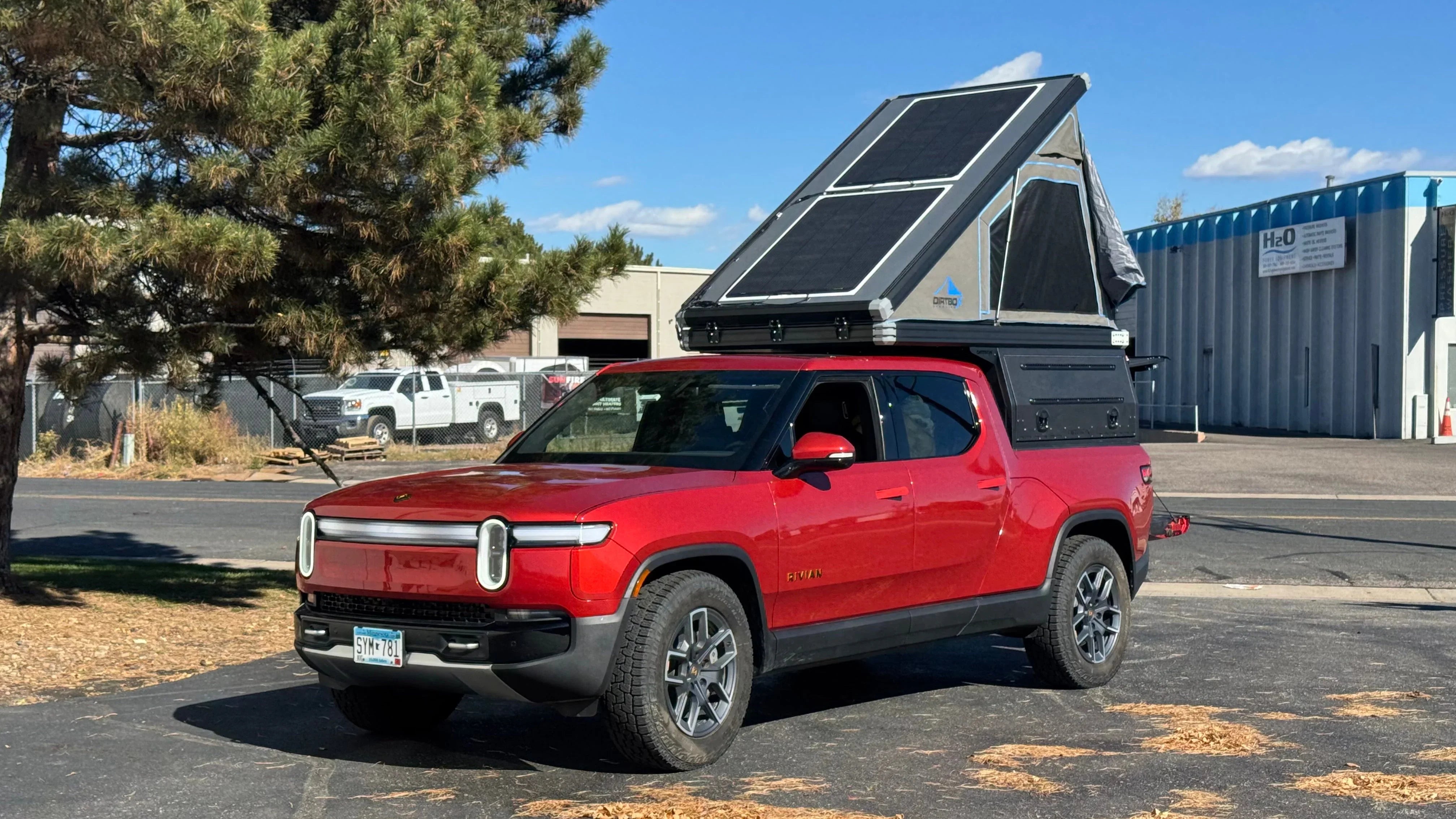 Red overland truck with rooftop tent and solar panels parked outdoors