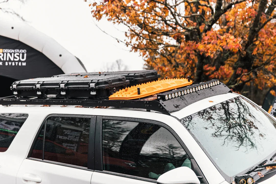 Toyota SUV with overlanding roof rack, recovery boards, gear case, and LED light bar in autumn