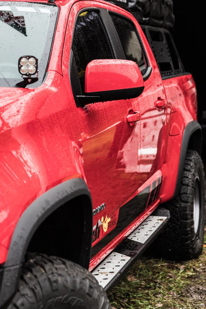 Red Toyota Tacoma with off-road tires, side step, roof rack, and overlanding accessories in rain