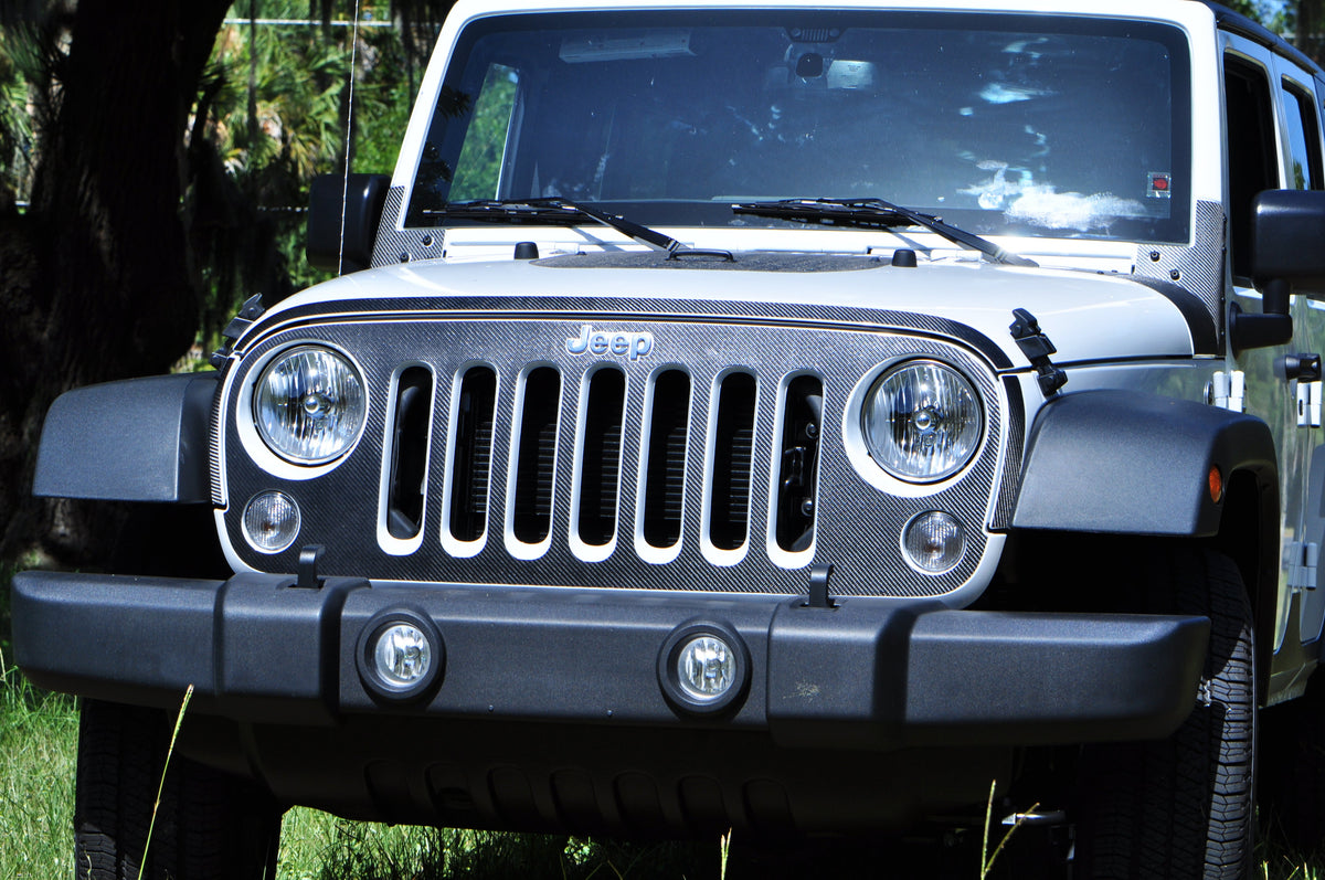 Front of a white Jeep Wrangler JK with a gray Tufskinz grill overlay behind the seven slots, black bumper and fog lights