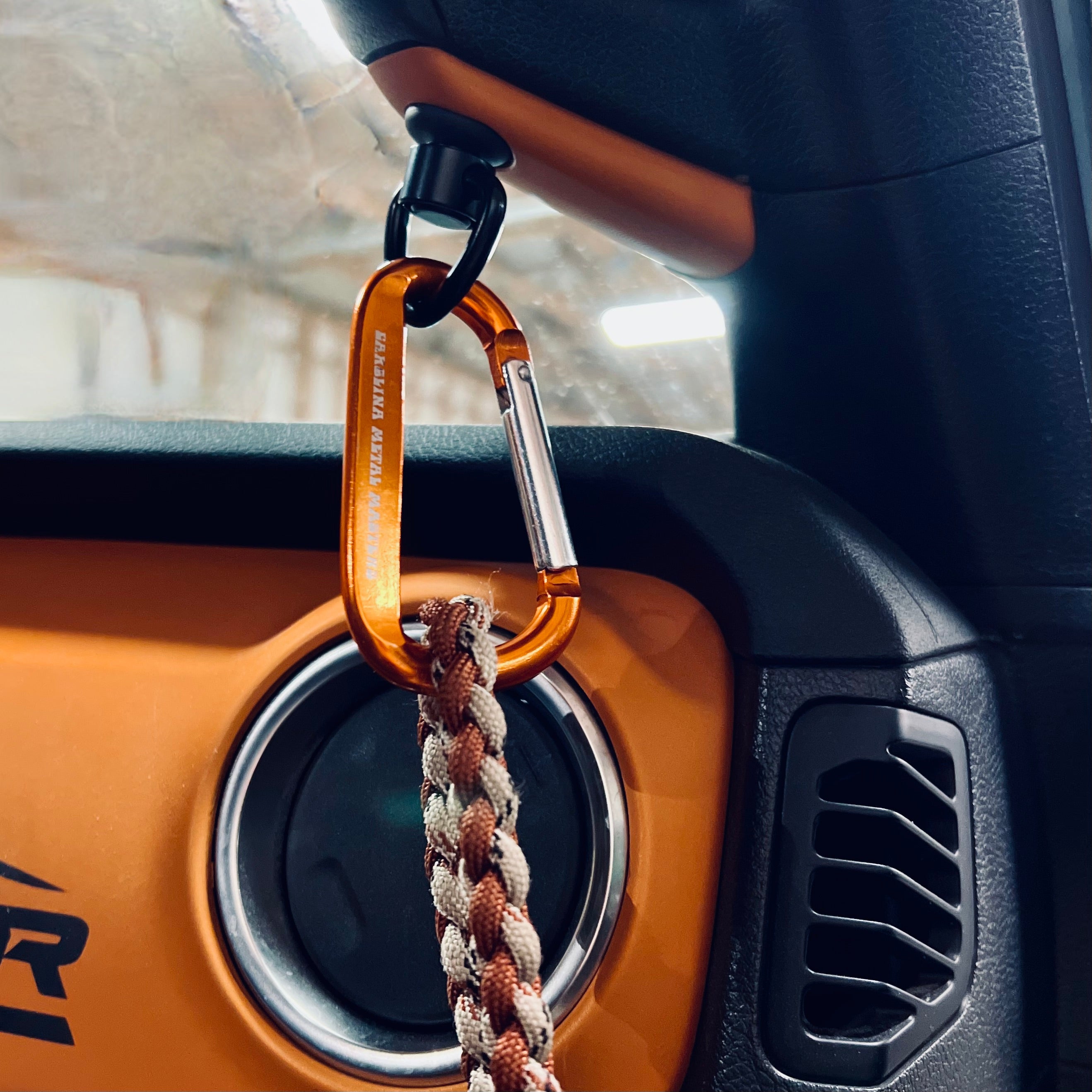 Orange carabiner clip with paracord attached to Jeep Wrangler grab handle in dashboard close-up.