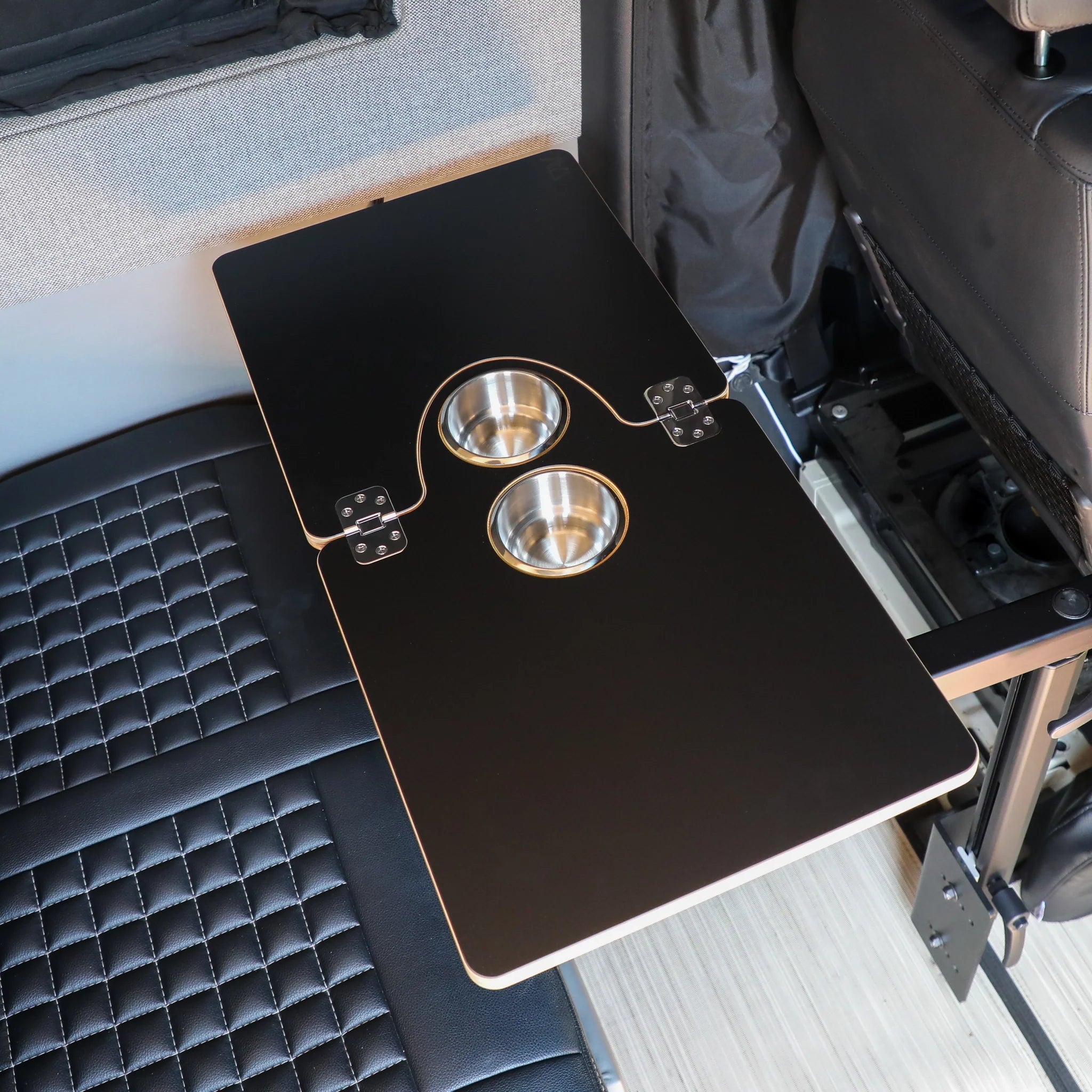 Fold-out vehicle camping table with dual cup holders, mounted beside quilted car seat