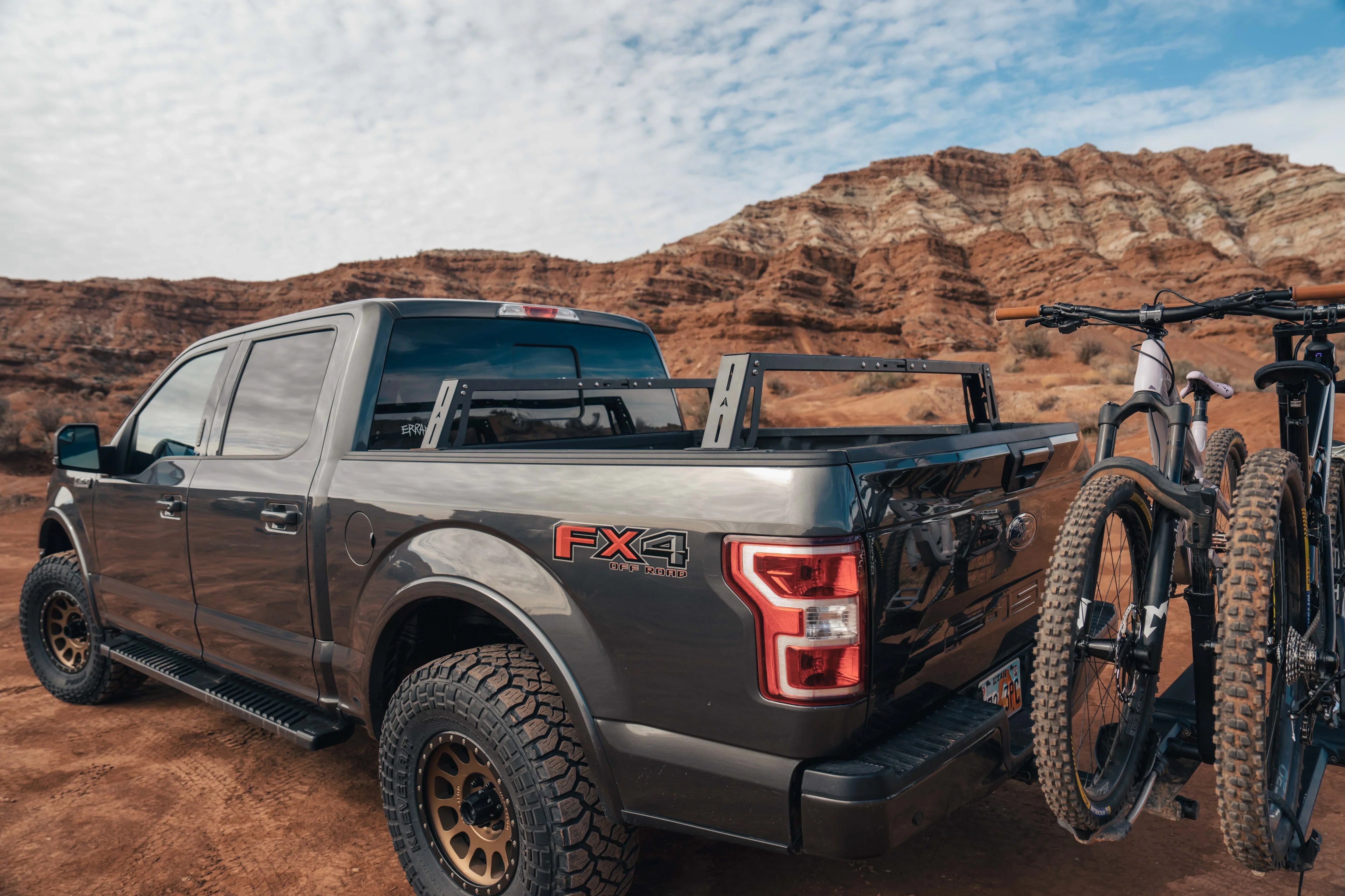 Off-road Ford FX4 truck with bed rack and bikes on hitch rack in desert landscape
