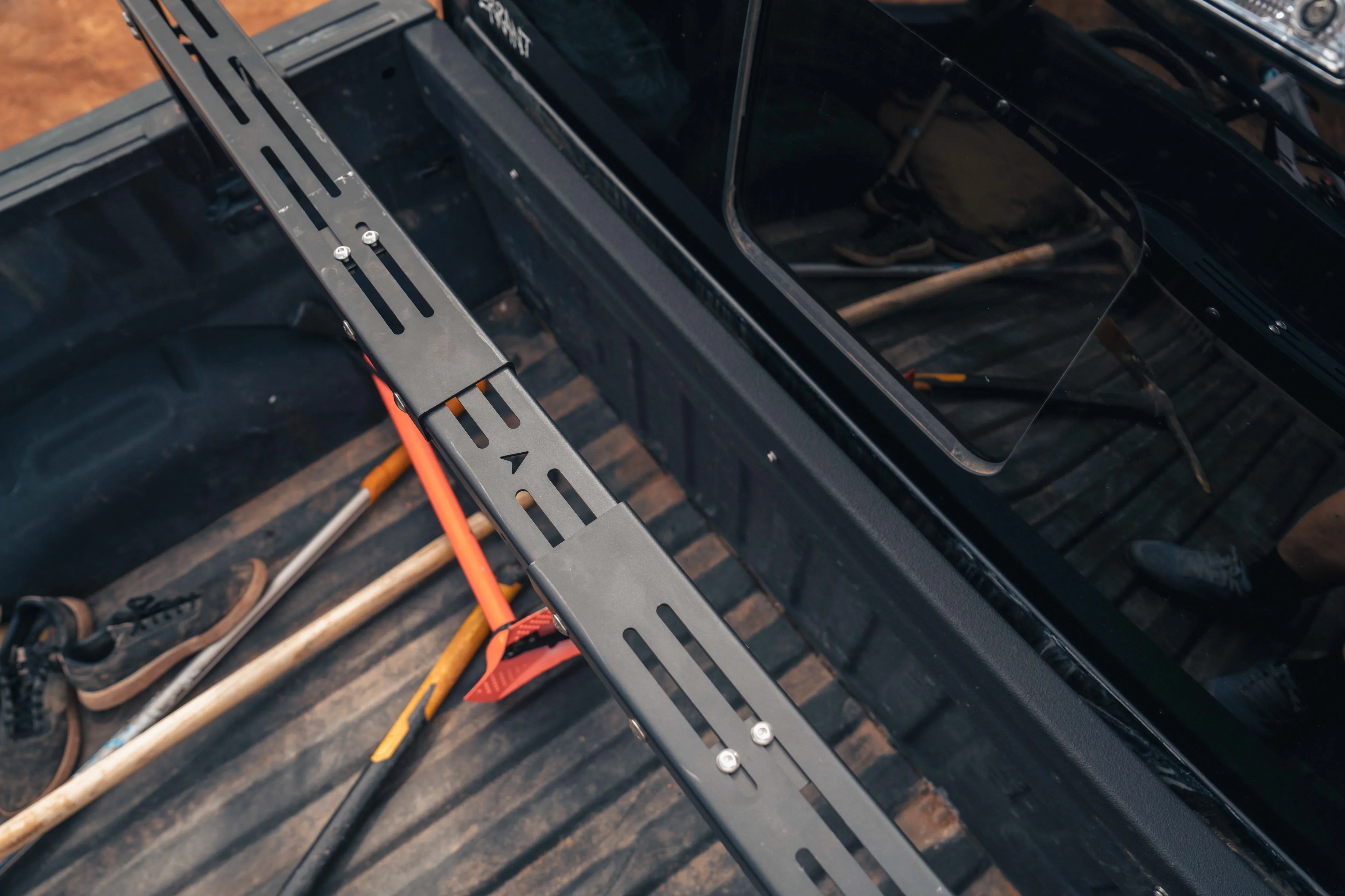 Adjustable bed rack crossbar installed in a pickup truck bed with overlanding tools