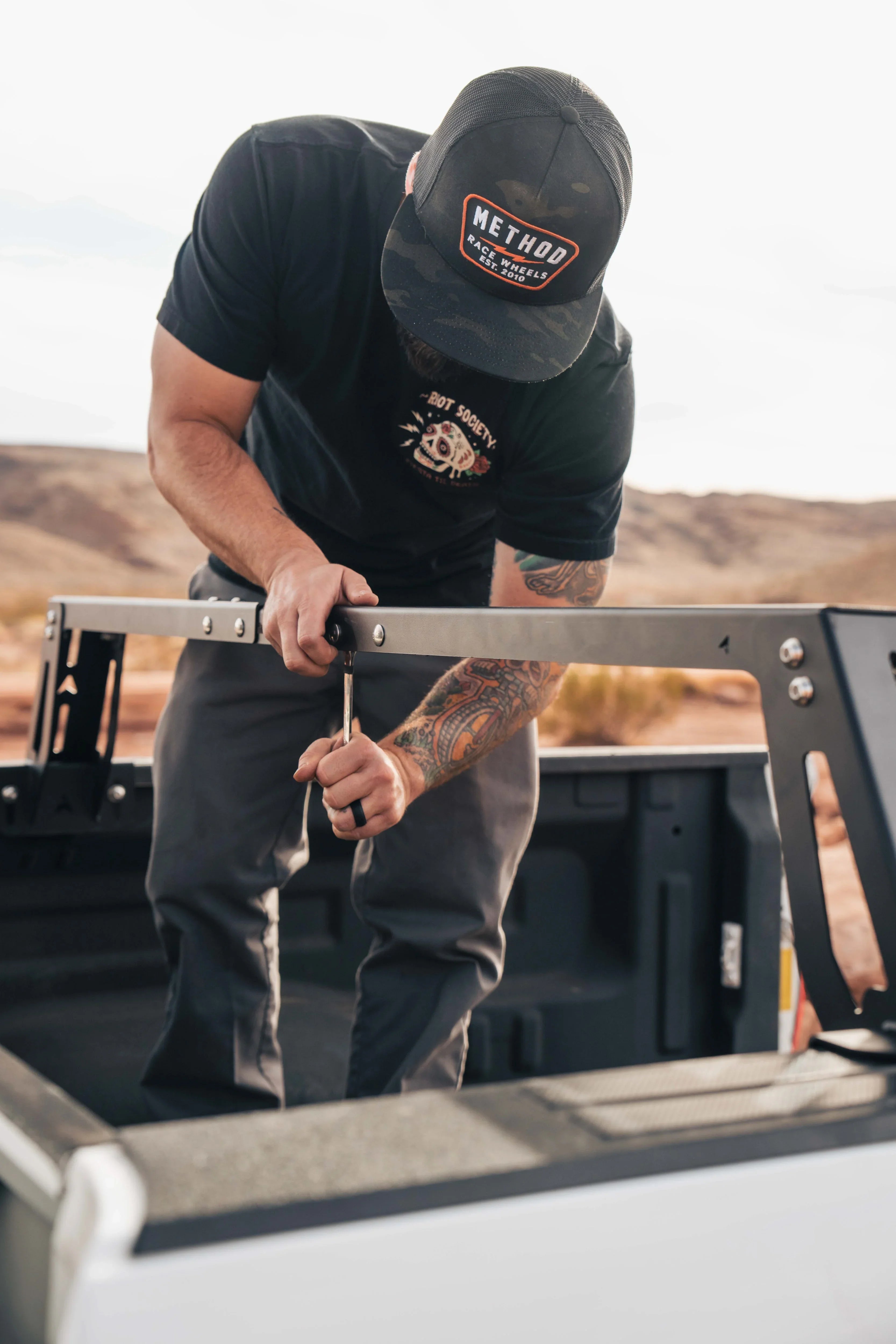 Man assembling overland bed rack on pickup truck in outdoor setting