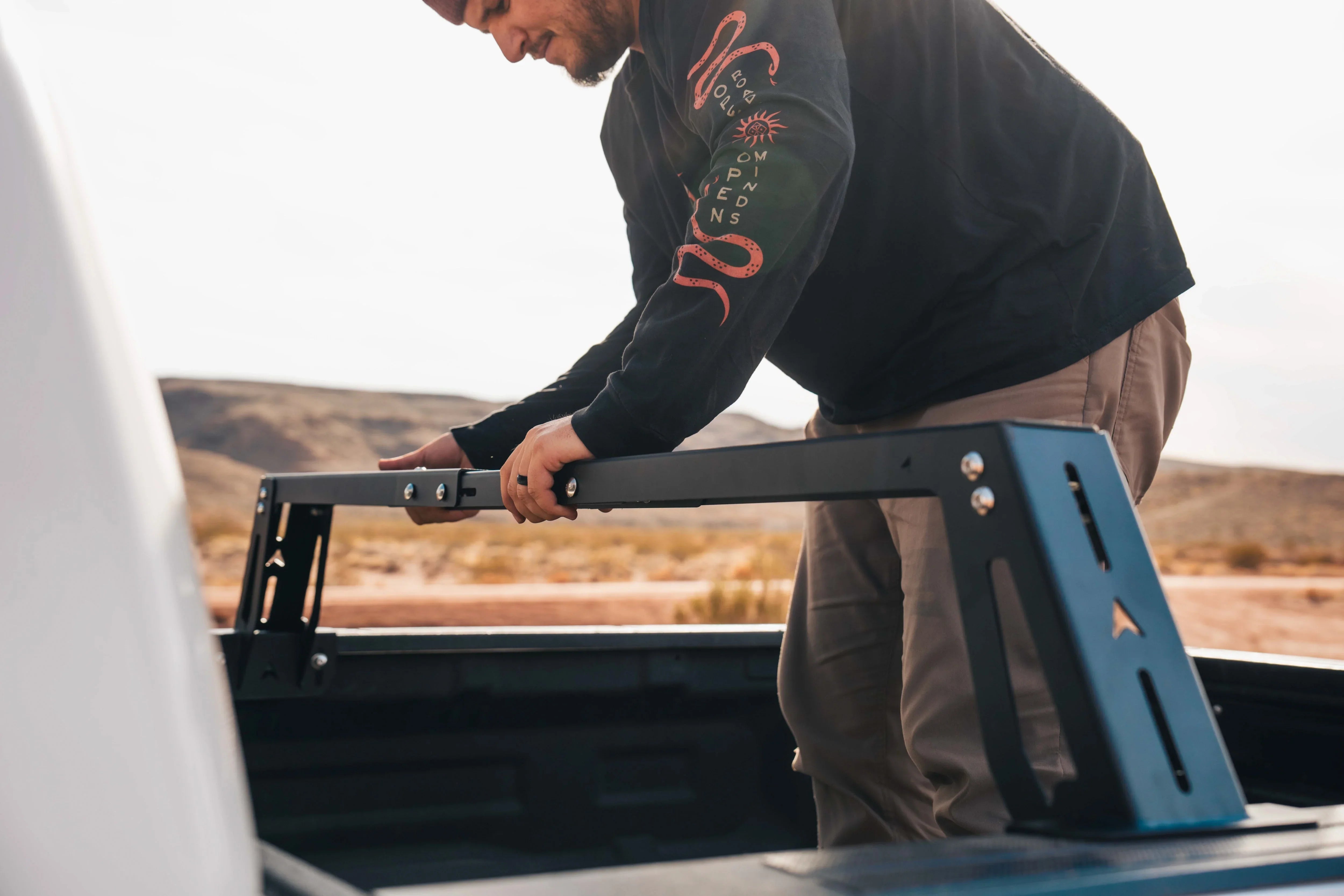 Man installing modular bed rack system on truck for overlanding or camping outdoors