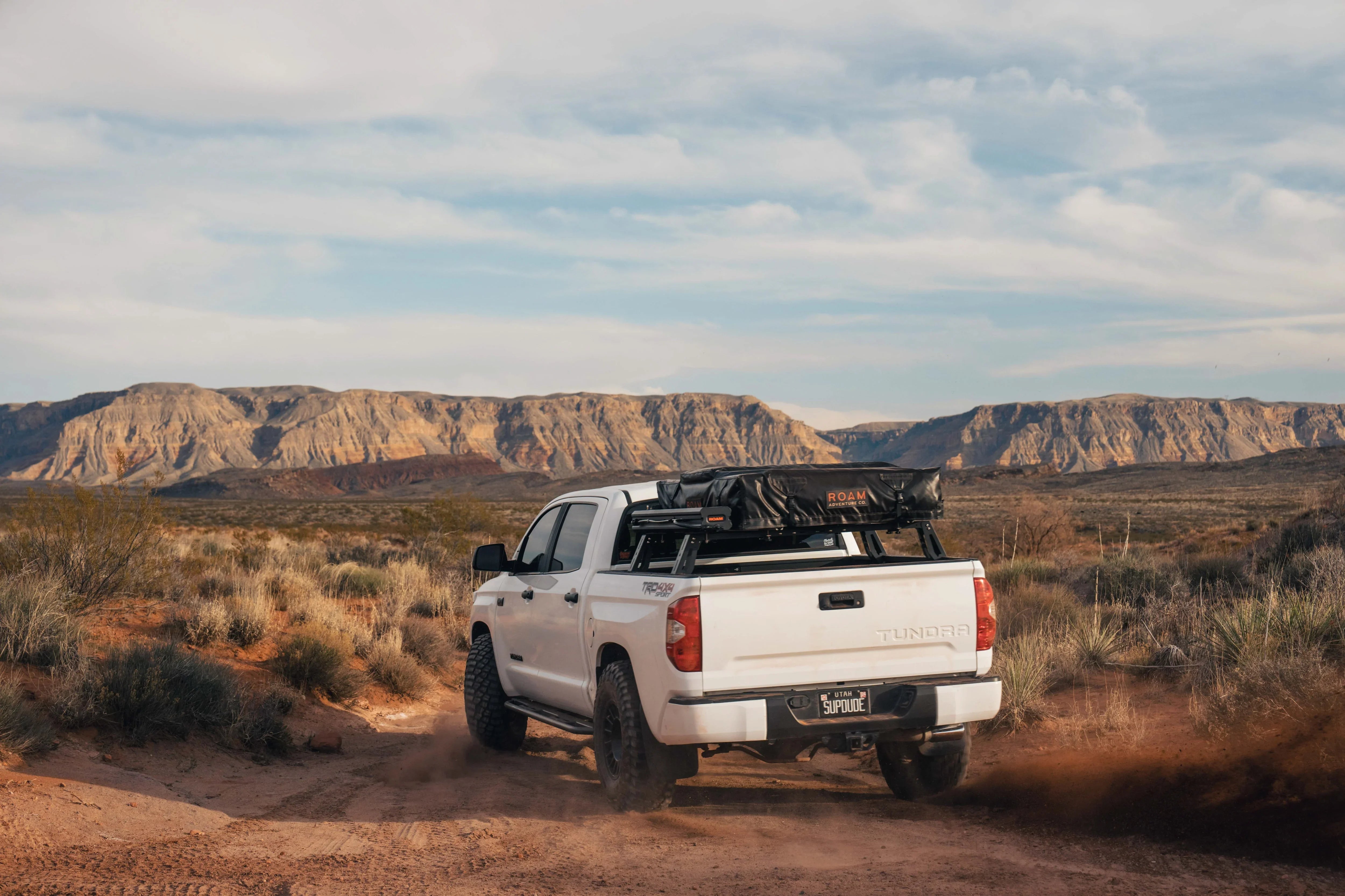 Toyota Tundra with off-road gear driving through desert landscape, mountains in background