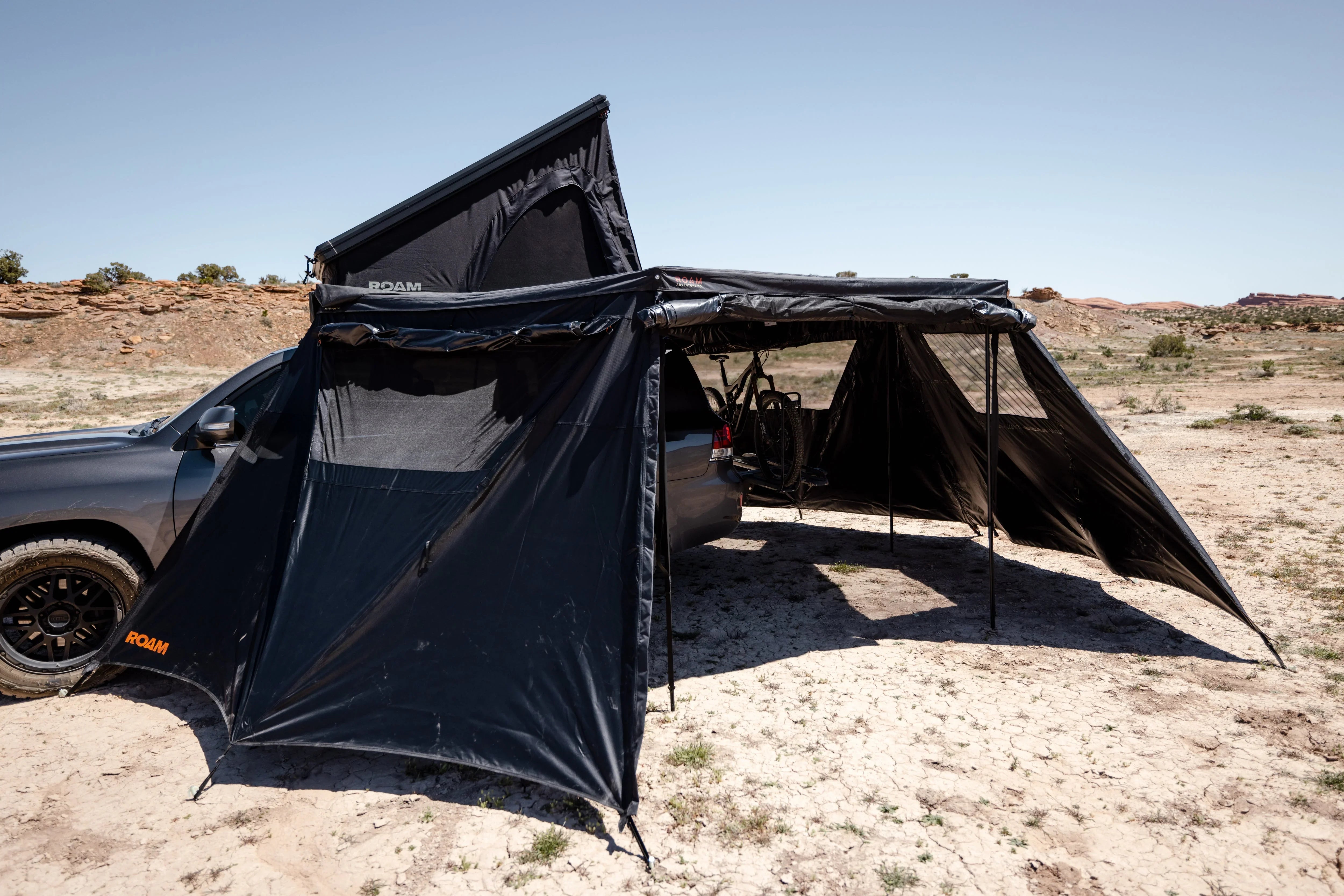 Black overlanding vehicle awning tent with rooftop tent set up in desert landscape