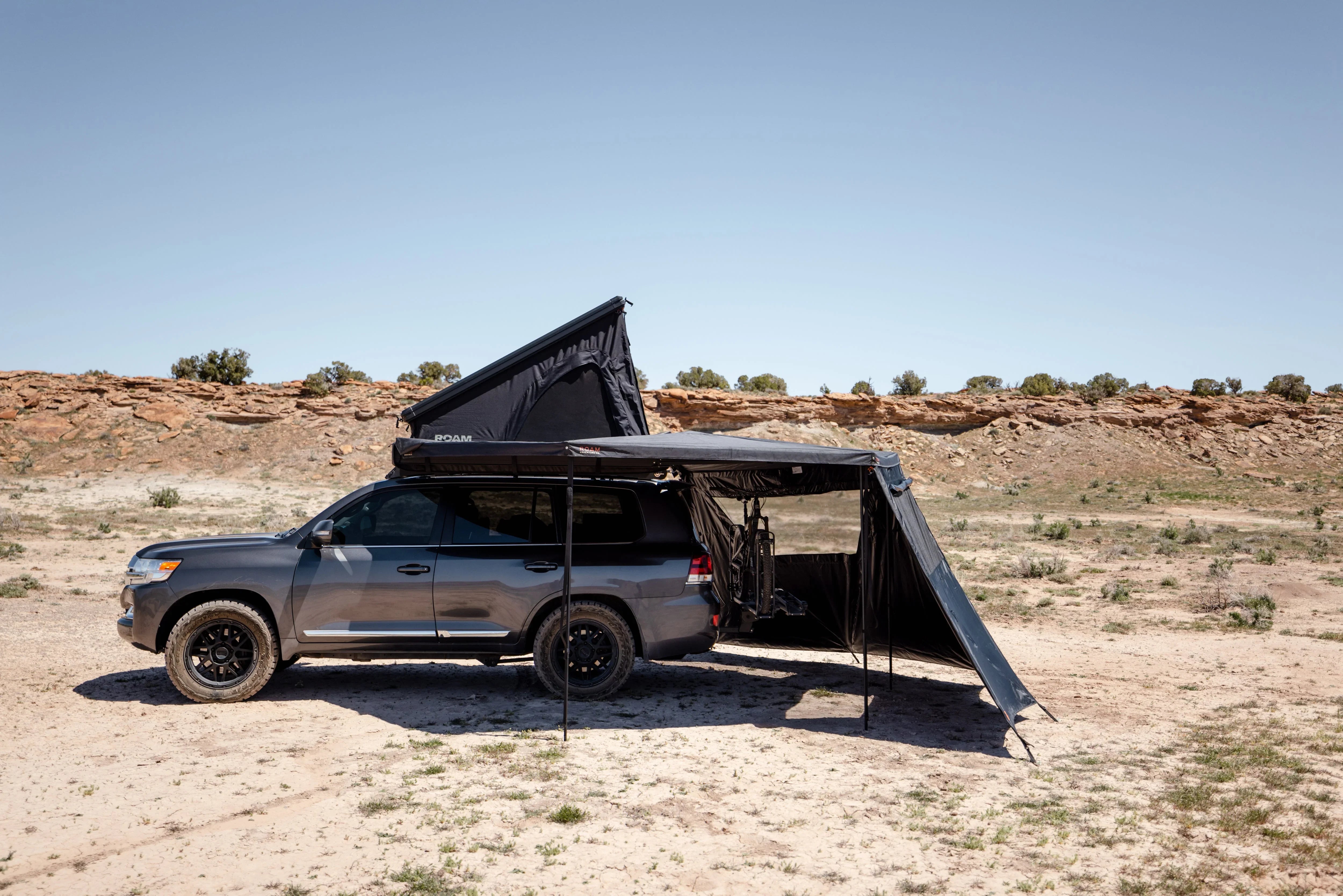 SUV with rooftop tent and awning set up for overlanding in desert landscape