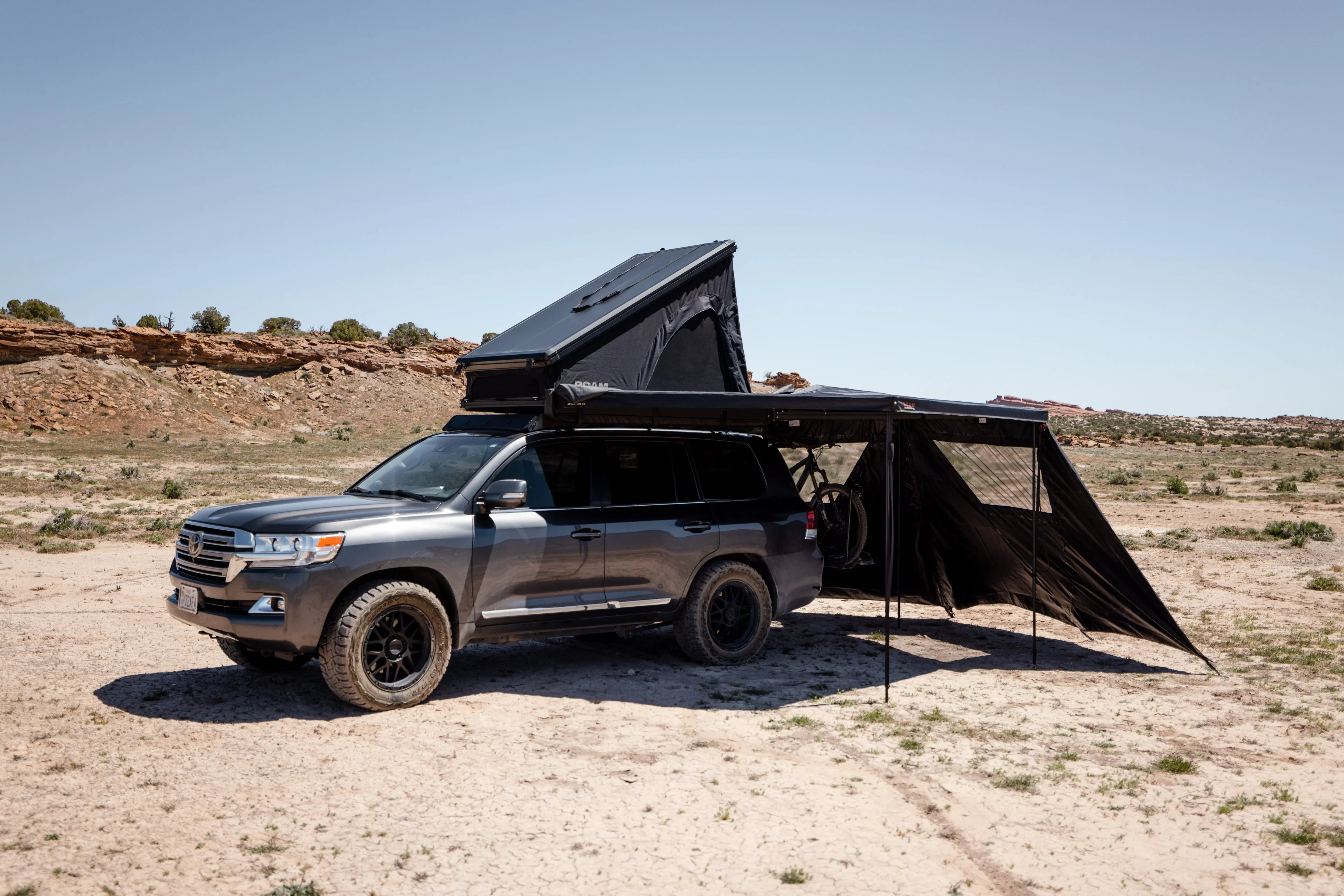 Overlanding SUV with rooftop tent and awning parked in a desert camping location