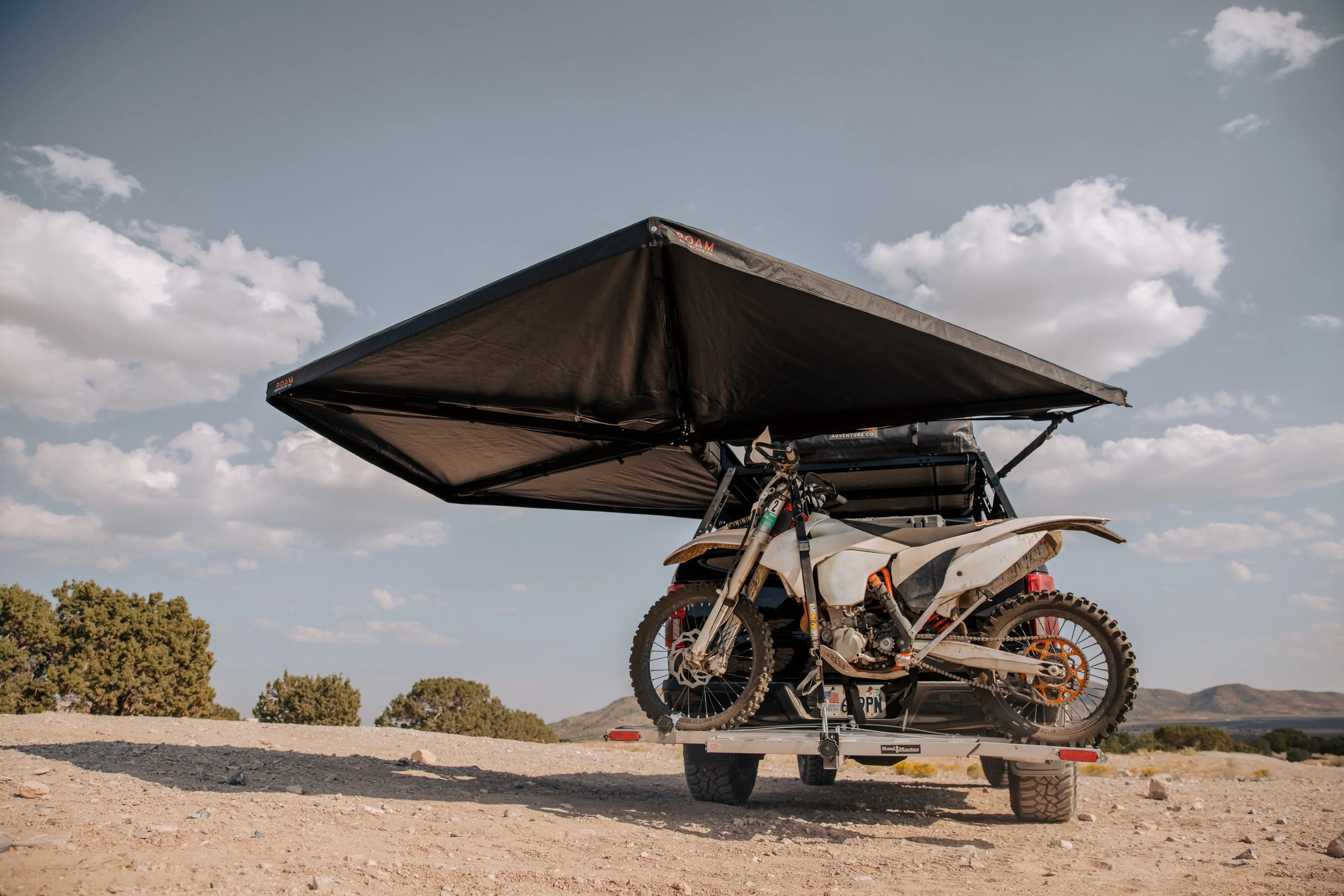 Overland vehicle with rooftop awning and dirt bike carrier parked on rocky terrain