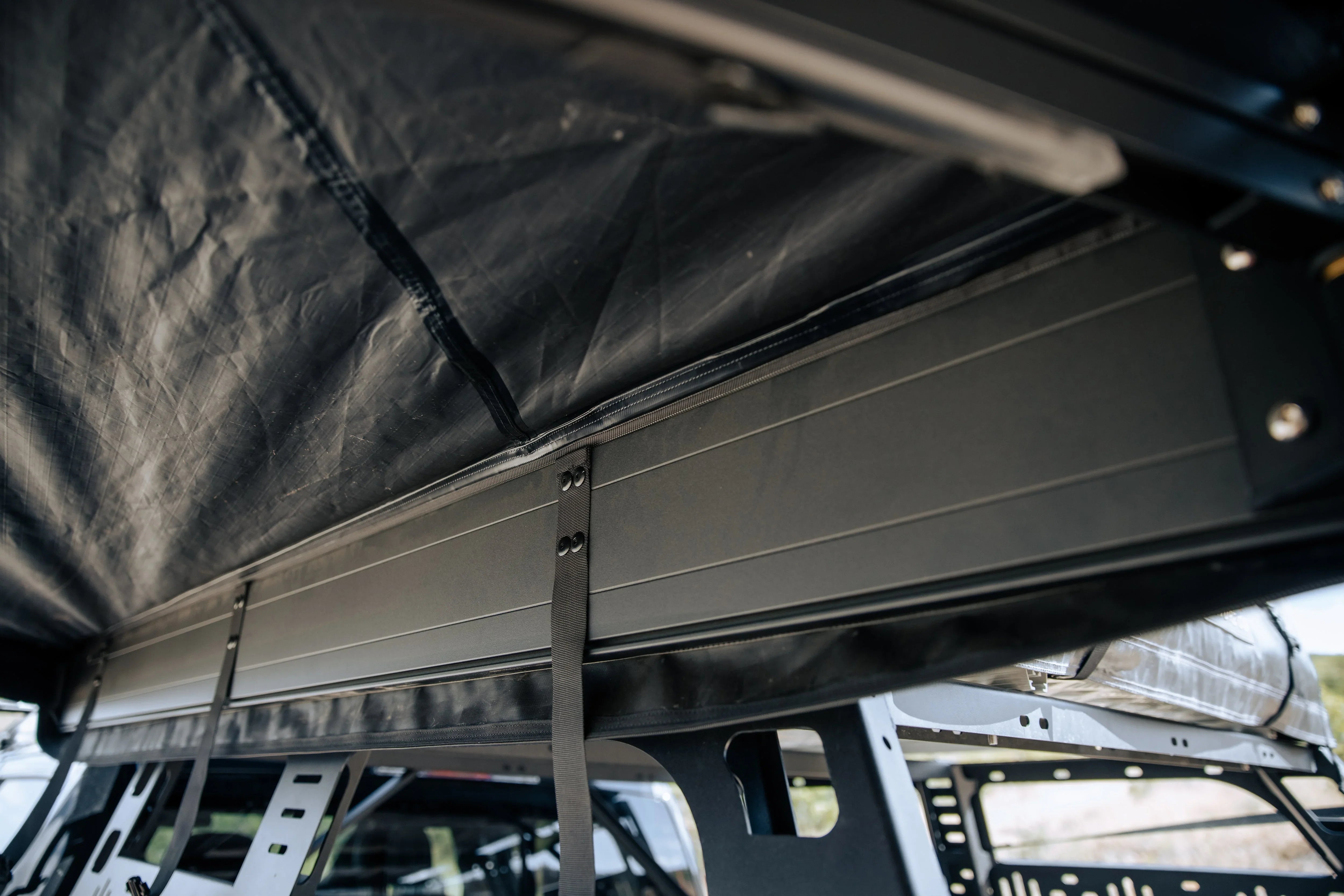 Close-up of a rooftop tent setup with black frame and straps for overlanding vehicles