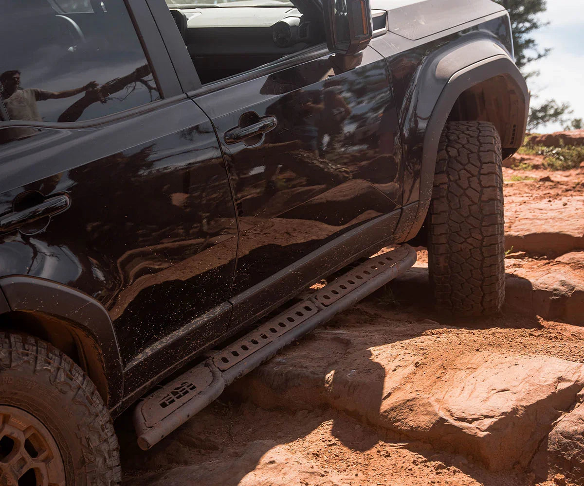Off-road vehicle with kickout rock sliders on rocky trail, overlanding accessory detail