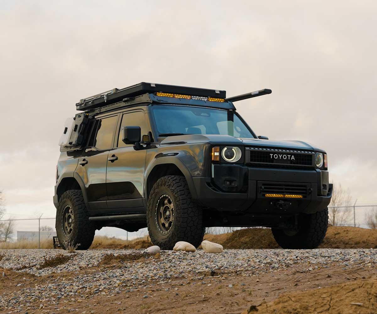 Toyota SUV with off-road tires and roof rack camping gear parked on gravel outdoors
