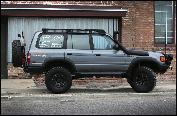 Toyota Land Cruiser SUV with overlanding accessories and roof rack parked by a brick wall