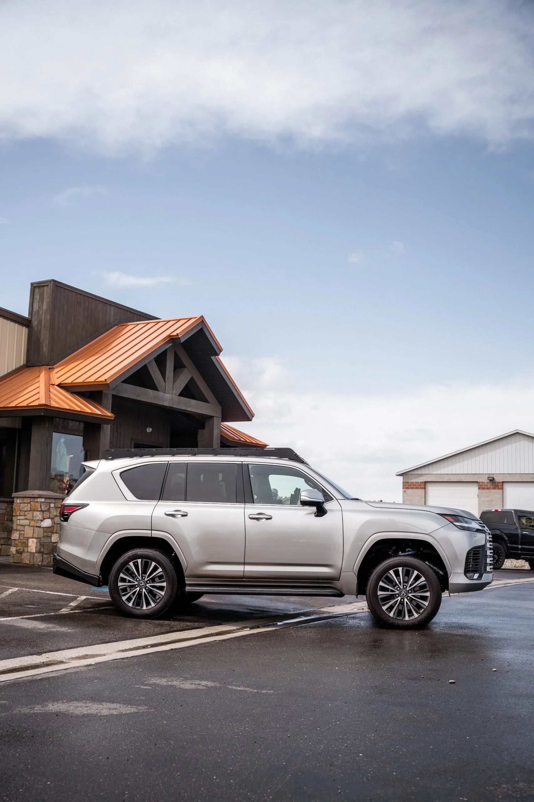 Silver Lexus LX600 SUV with roof rack parked outside a rustic building, ready for overlanding.
