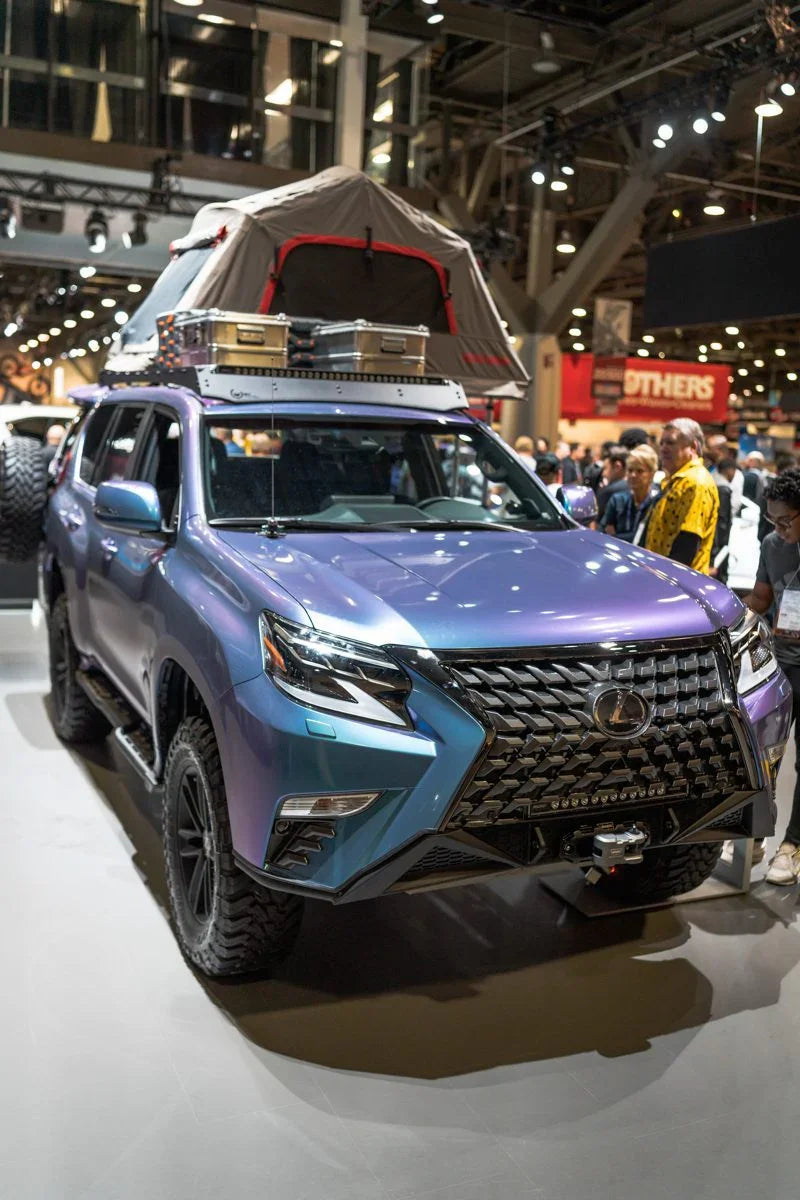 Lexus GX460 SUV with rooftop tent, storage boxes, and off-road gear at indoor expo.