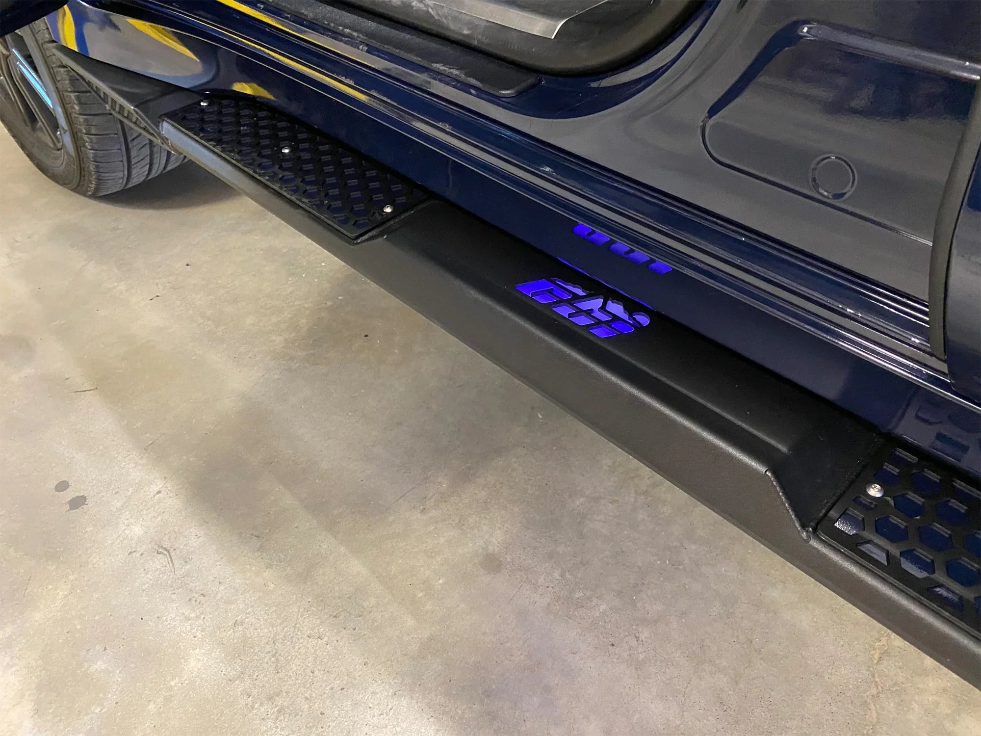 Lexus LX 570 aftermarket rock sliders with step and blue LED lights, garage setting