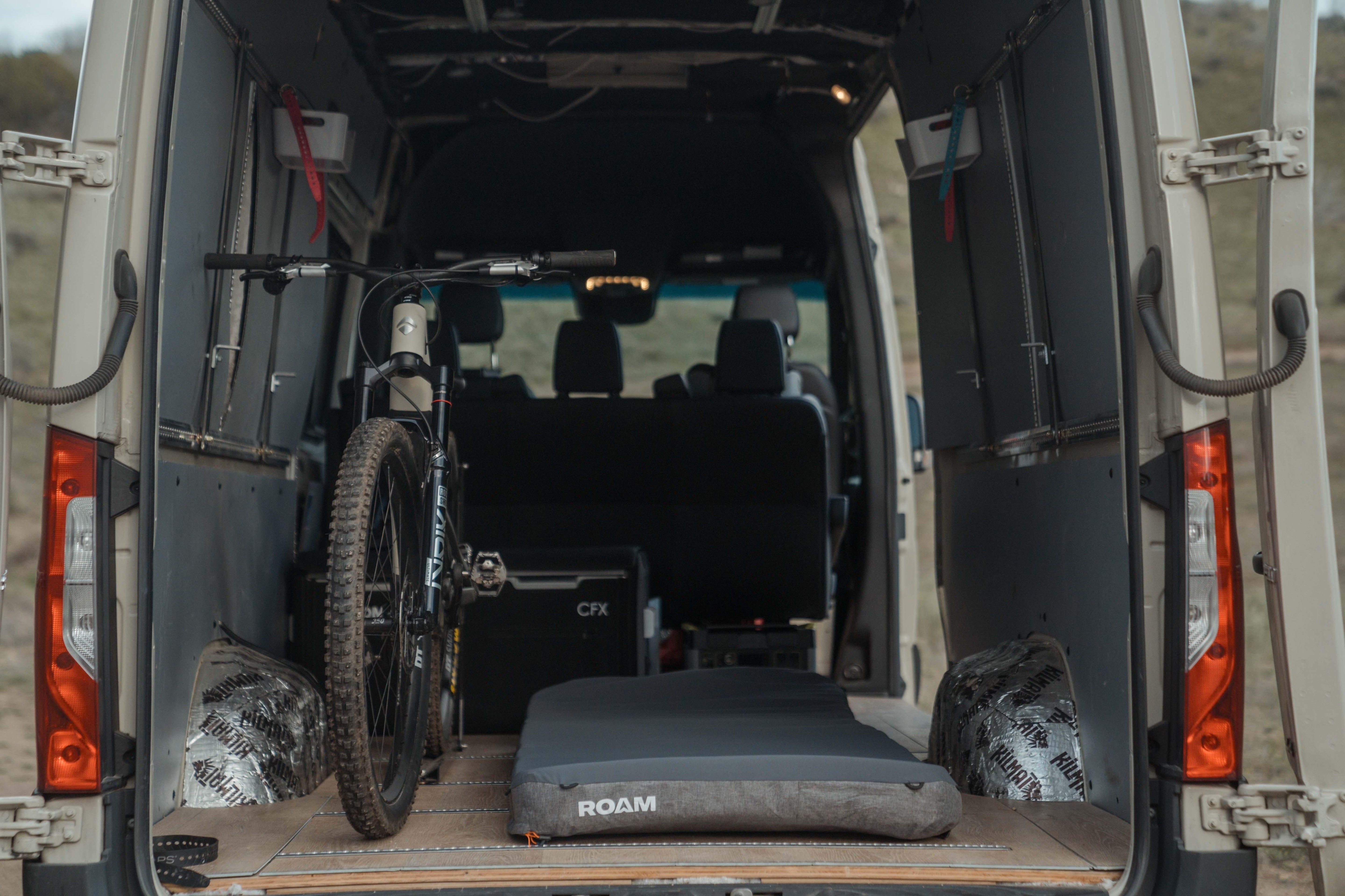 Van interior setup with bike, camping mattress, and overlanding gear for adventure travel