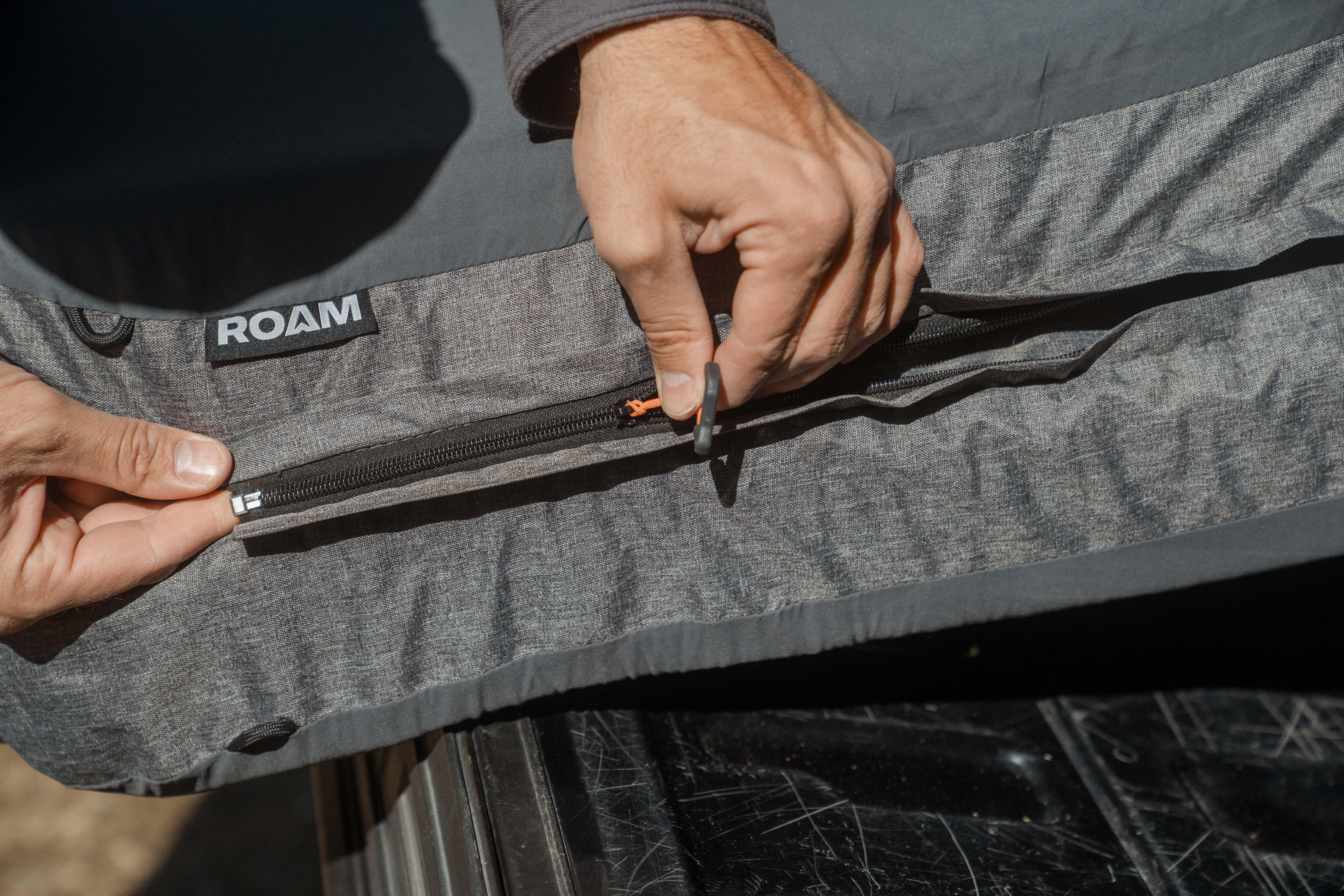 Close-up of hands unzipping gray ROAM overland camping mattress cover outdoors