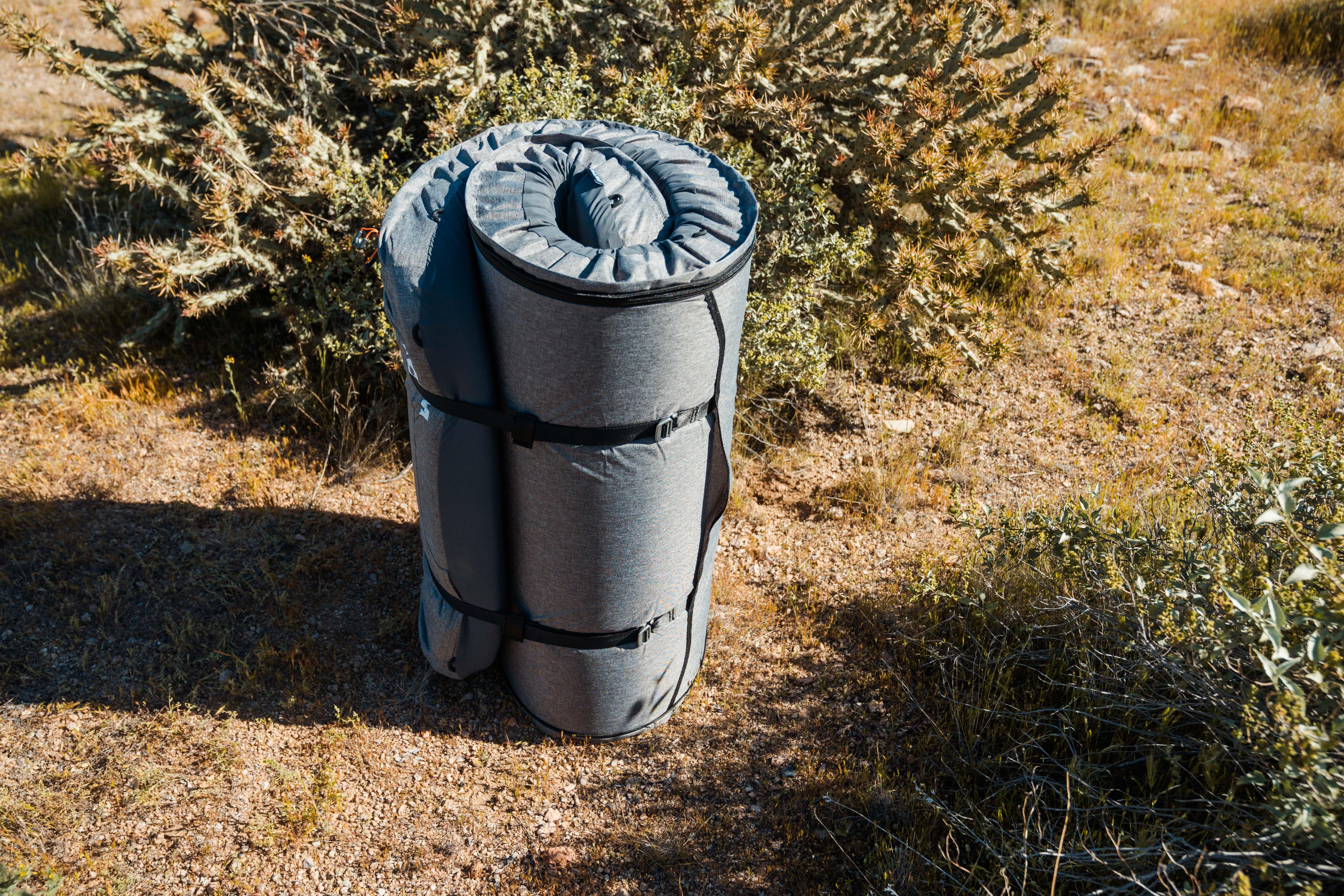 Rolled up camping mattress with straps on desert ground, outdoor overlanding gear