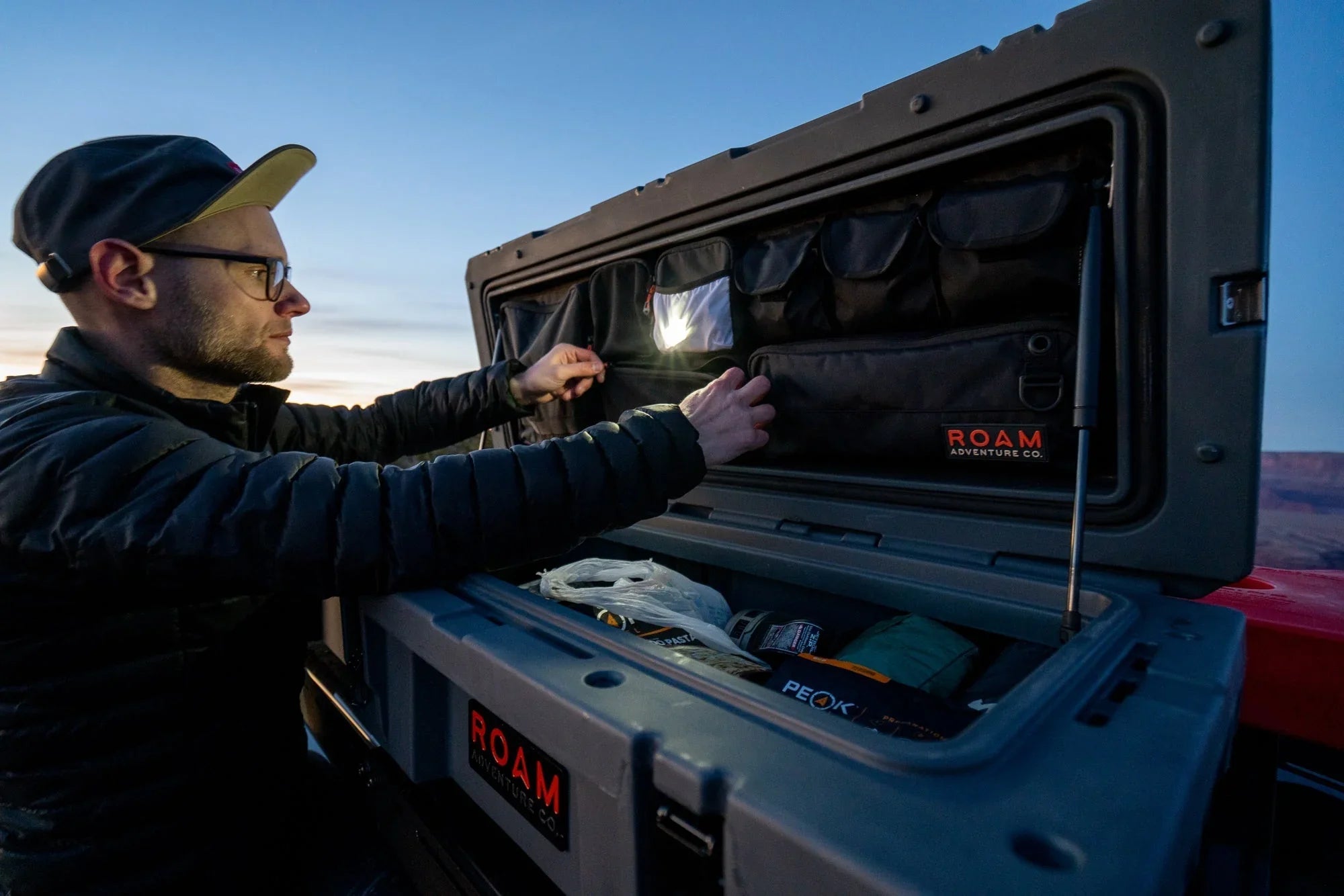 Man organizing camping gear in ROAM overlanding storage box at sunset outdoors