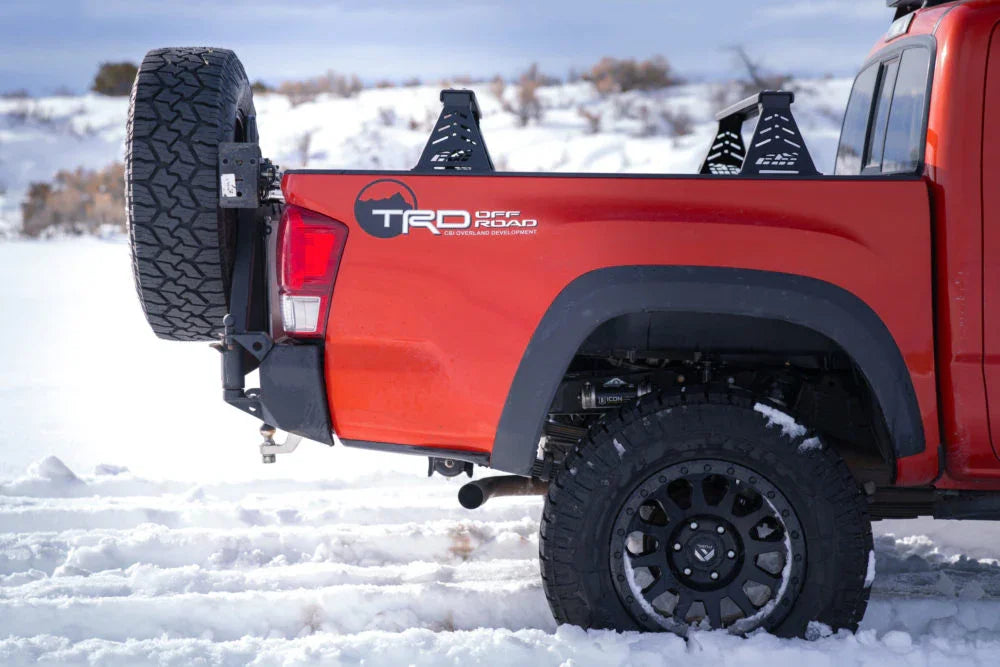 Red Toyota Tacoma TRD Off-Road with bed bars, mounted spare tire, in snowy terrain