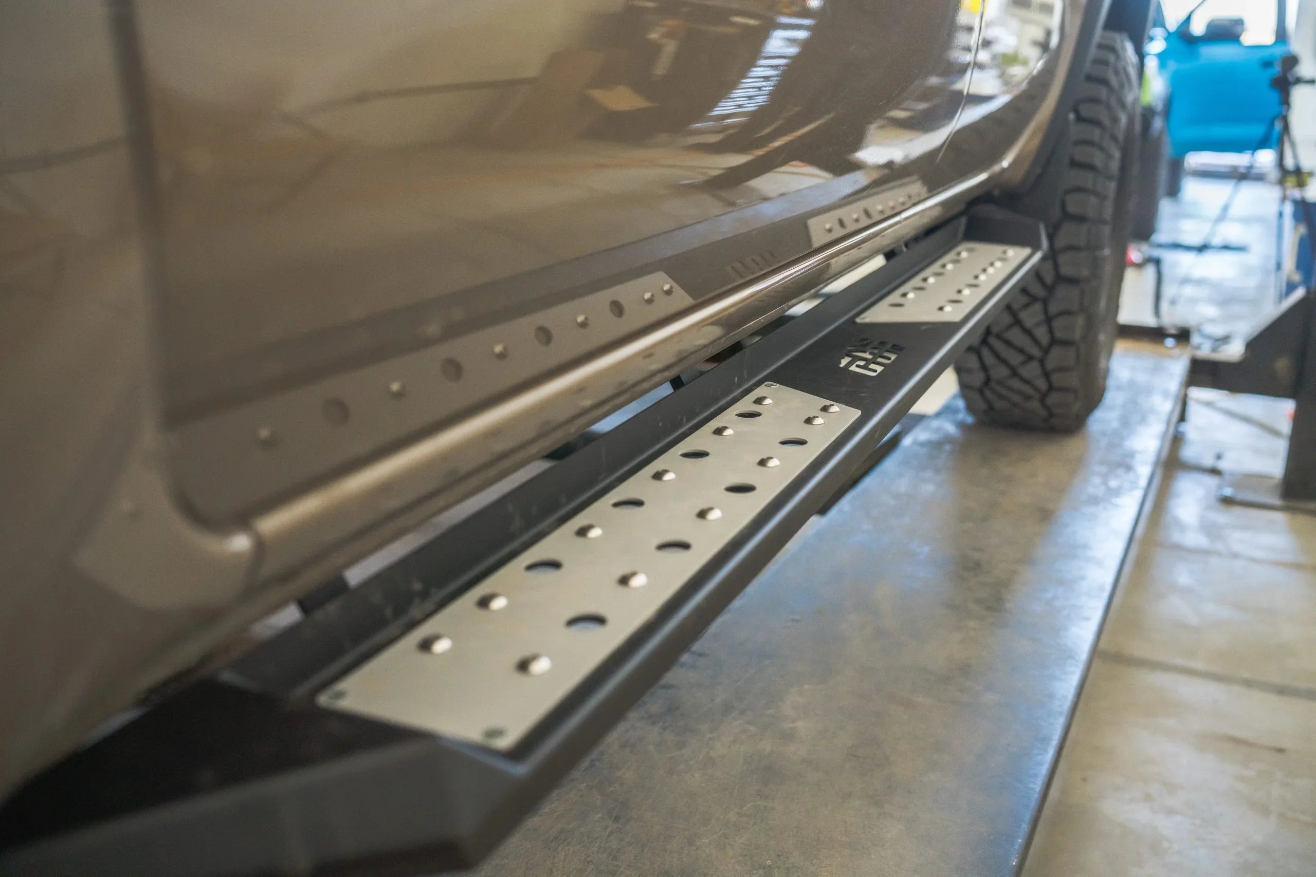 Close-up of off-road truck side steps and rugged all-terrain tires in garage setting